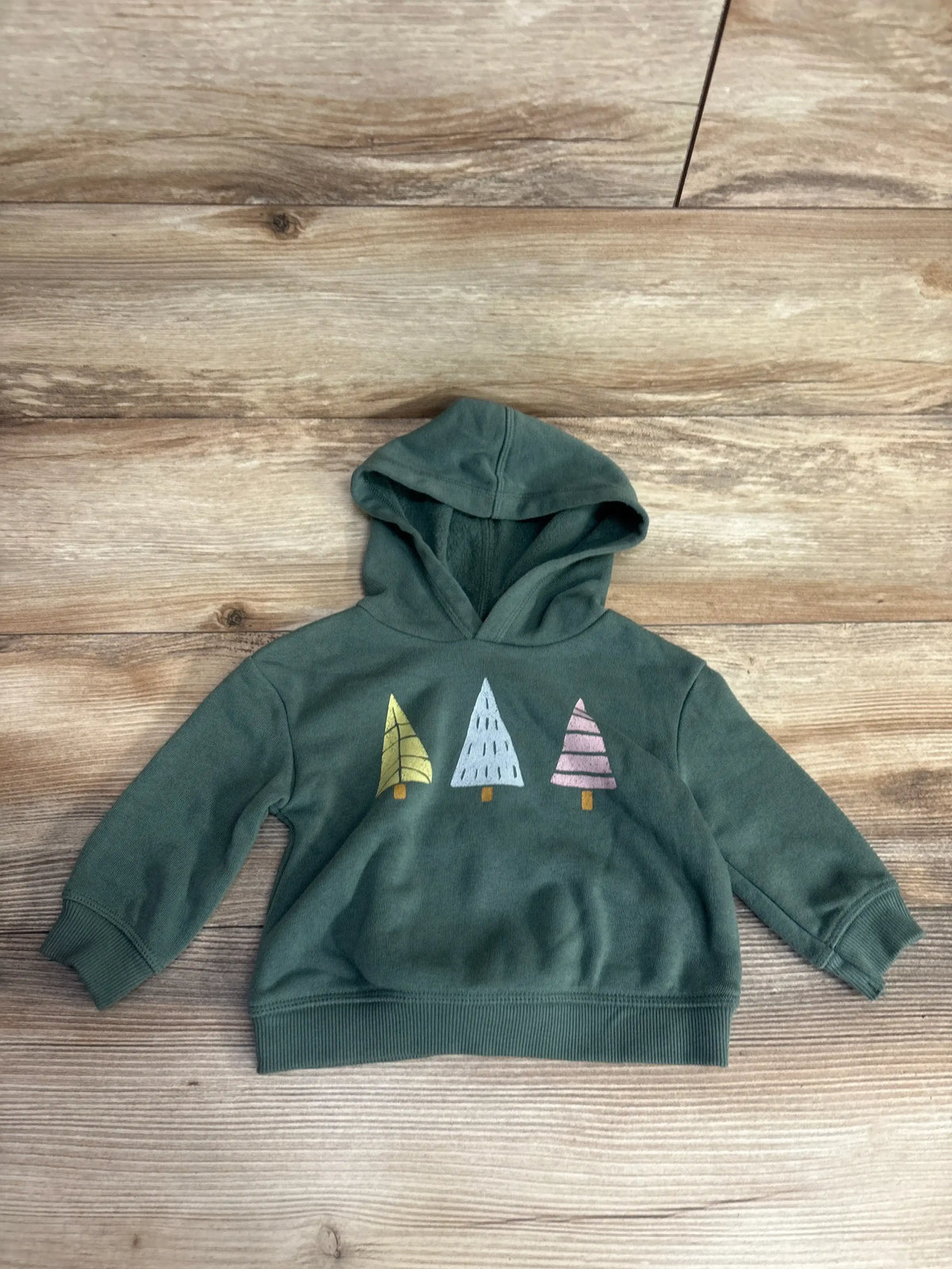Green kids' hoodie with three colorful tree graphics on wooden background