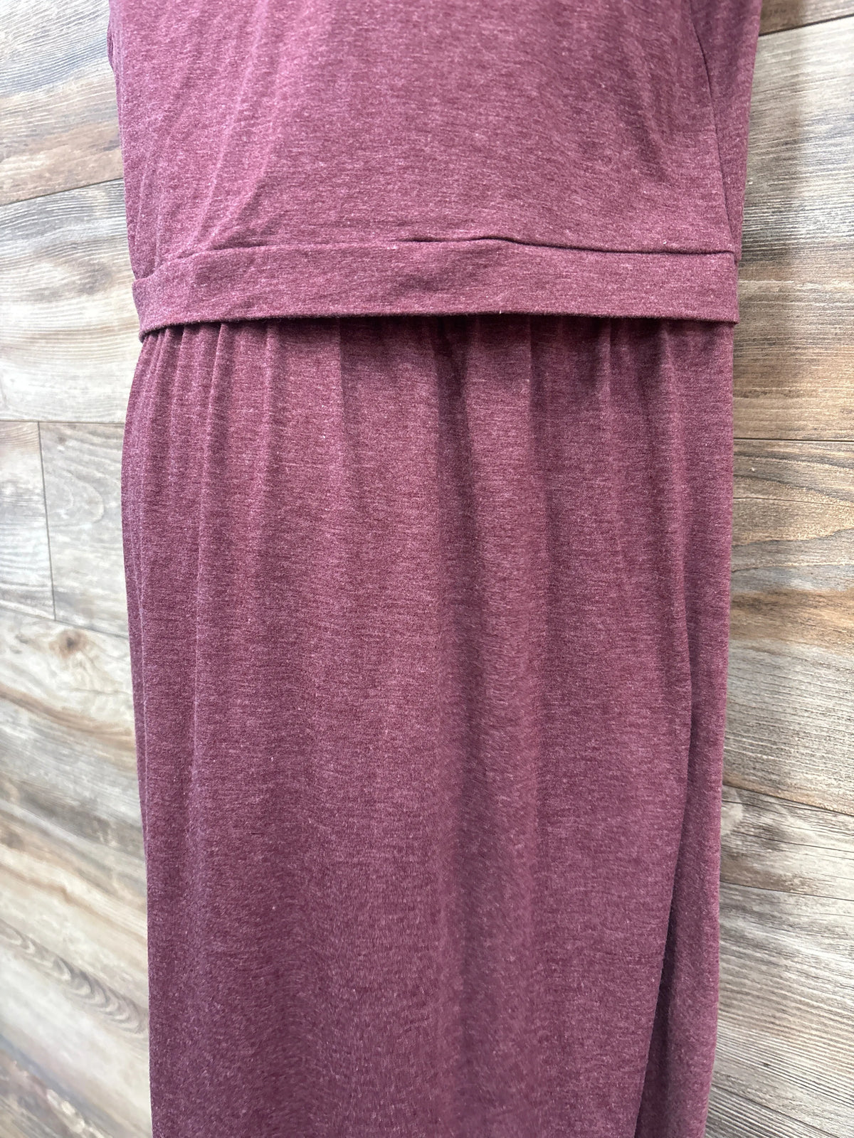 Close-up view of Plussiva maternity sleeveless nursing dress in maroon, showcasing gathered skirt and waist seam on a wood floor