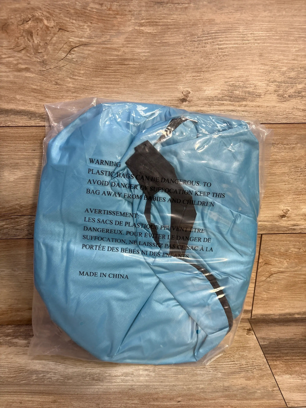 Top-down view of folded blue Monobeach pop-up baby sun tent in clear packaging showing black carry strap on wood floor
