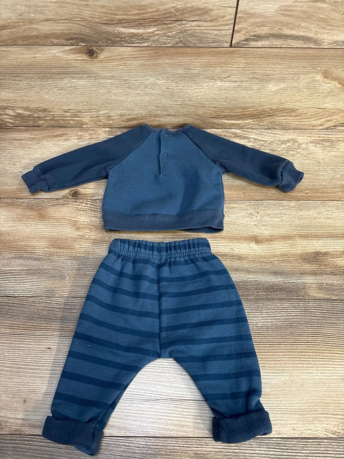 Blue baby boy outfit with long sleeve henley top and striped pants, laid flat on wood floor