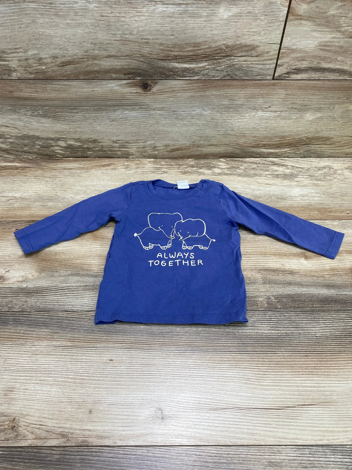 Front view of blue H&M baby long-sleeve shirt with white elephant graphic and ALWAYS TOGETHER text on wooden floor background