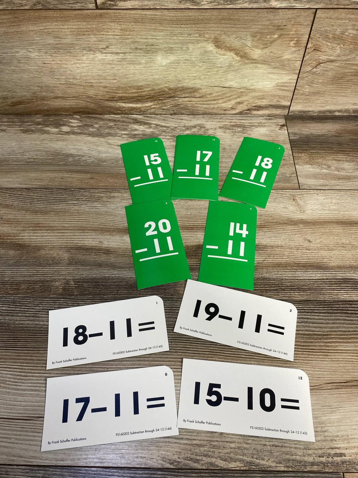 Top view of Frank Schaffer Publications subtraction flash cards showing green answer cards and white problem cards on wood
