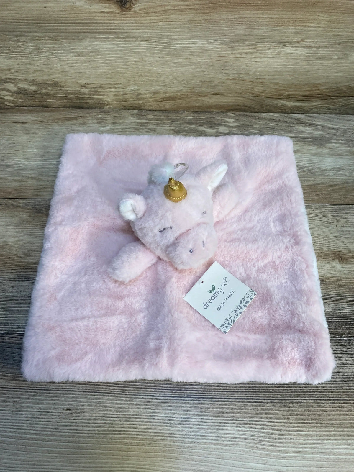 Plush pink unicorn security blanket for babies on wood background, soft cuddle toy