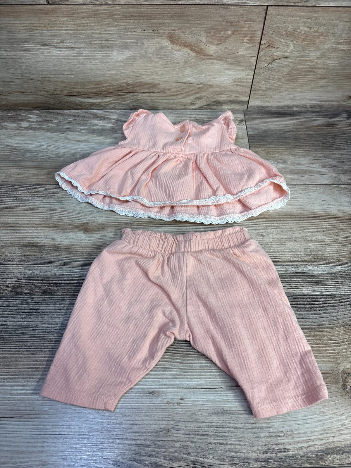 Flat lay of newborn peach Nicole Miller 2-piece gauze peplum top with lace trim and matching elastic-waist pants on wooden background