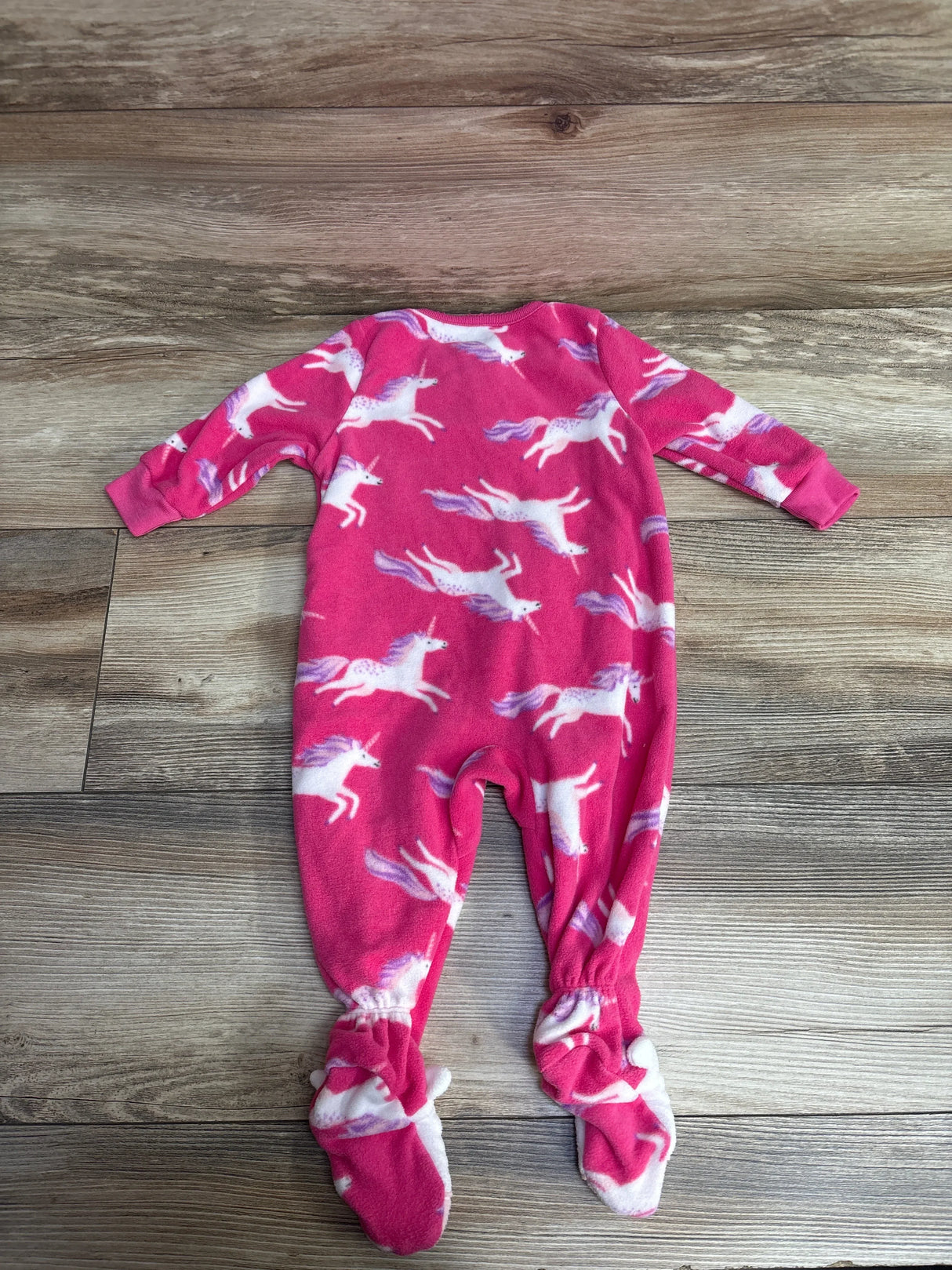 Pink baby fleece onesie with white and purple unicorn pattern laid flat on wooden floor