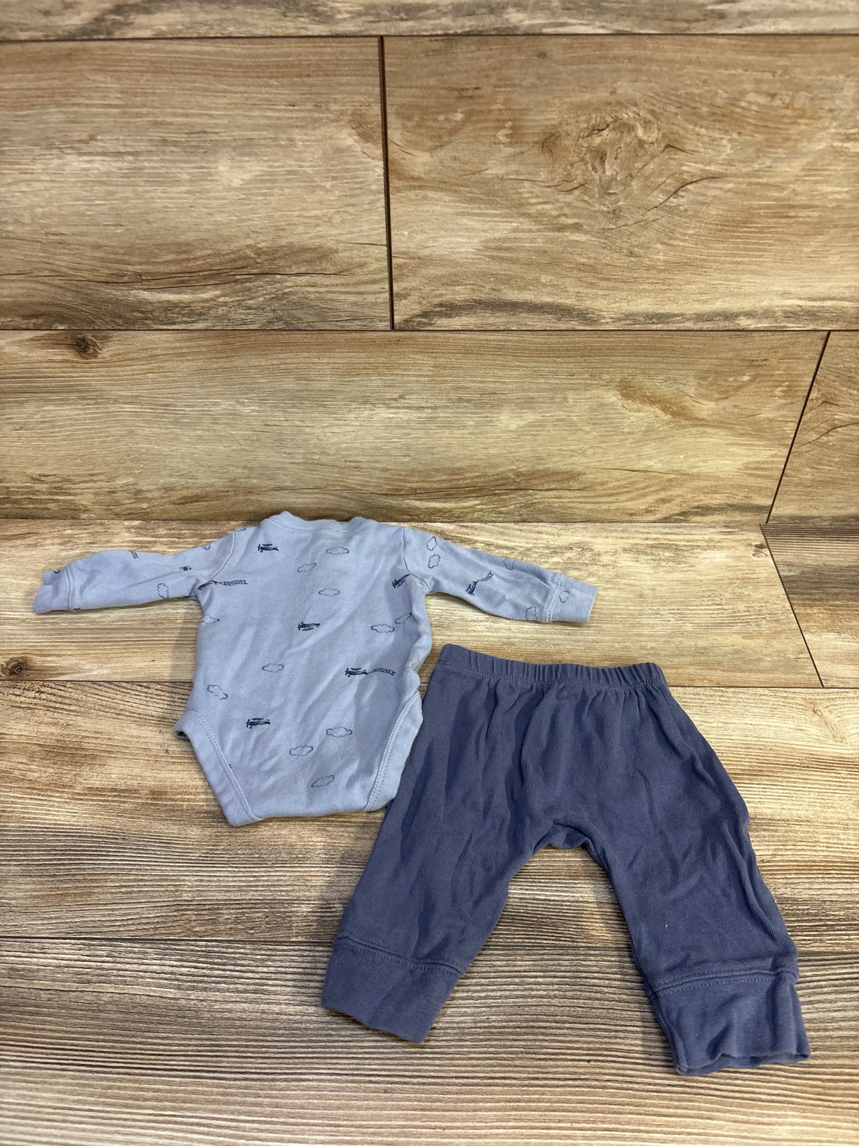 Flat lay of Just One You newborn blue long-sleeve bodysuit with cloud and plane print and navy pants on wood background