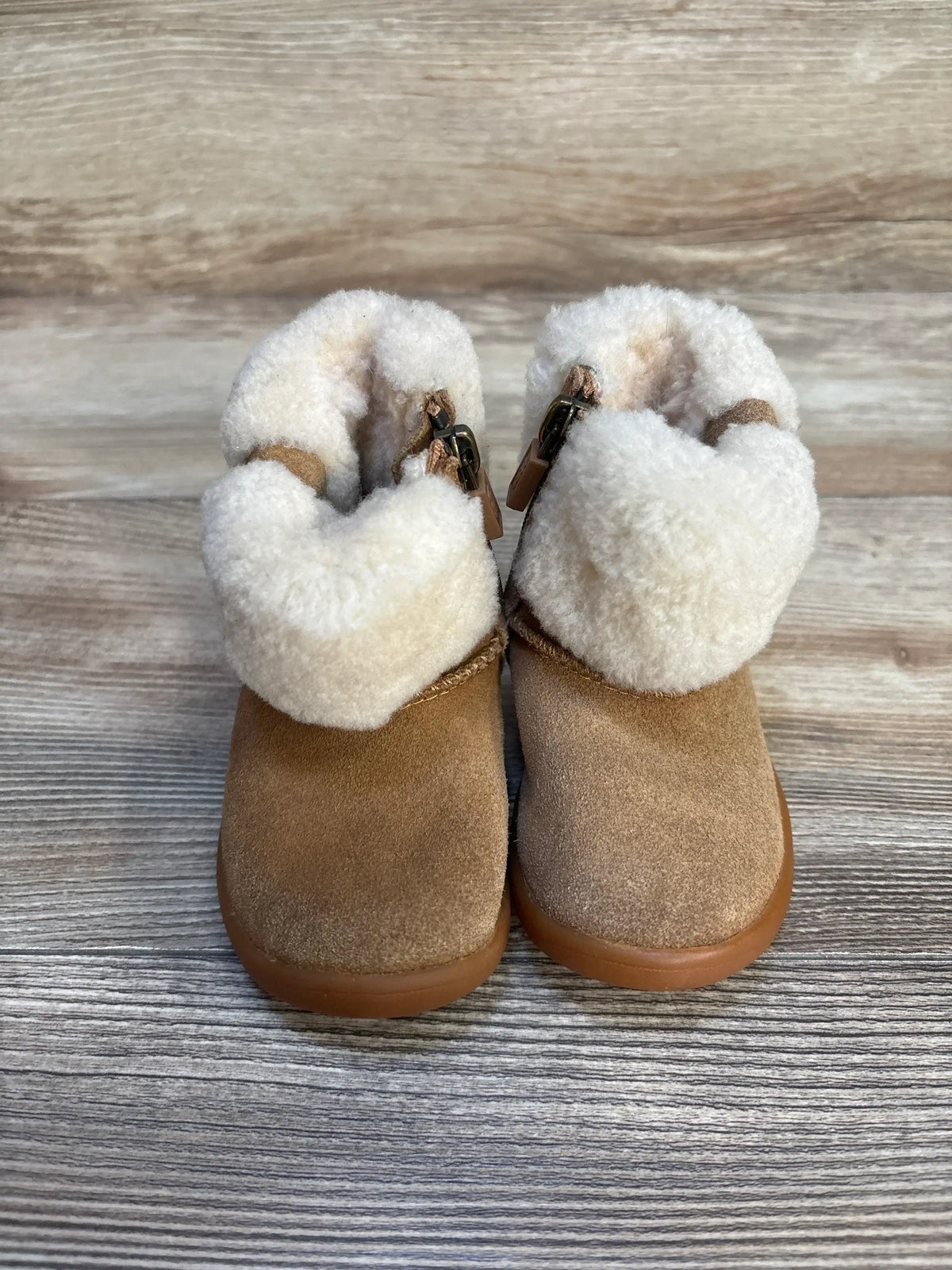Tan suede baby boots with white faux fur lining on wood background