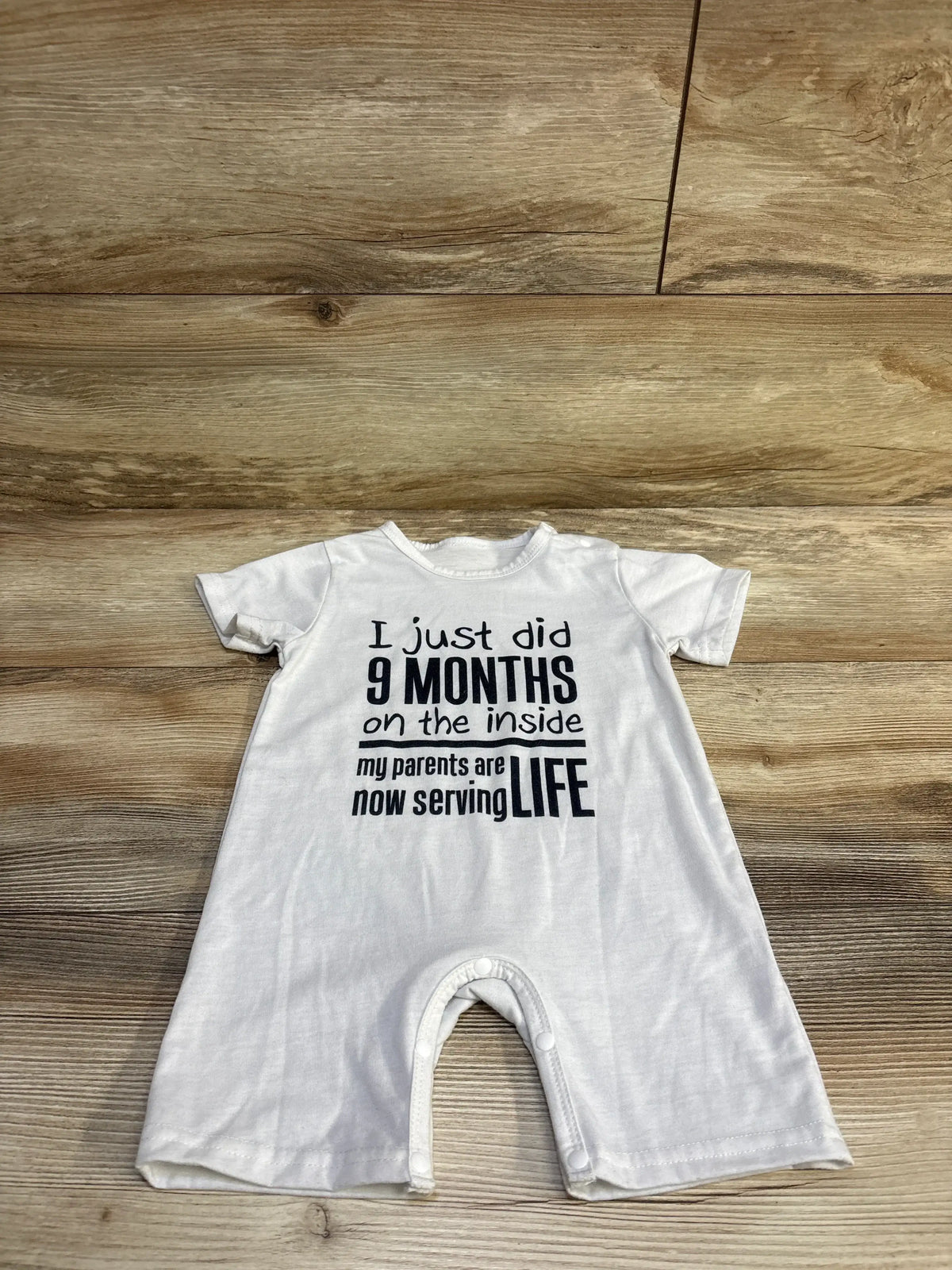 White baby romper with the text 'I just did 9 MONTHS on the inside' on a wood background.