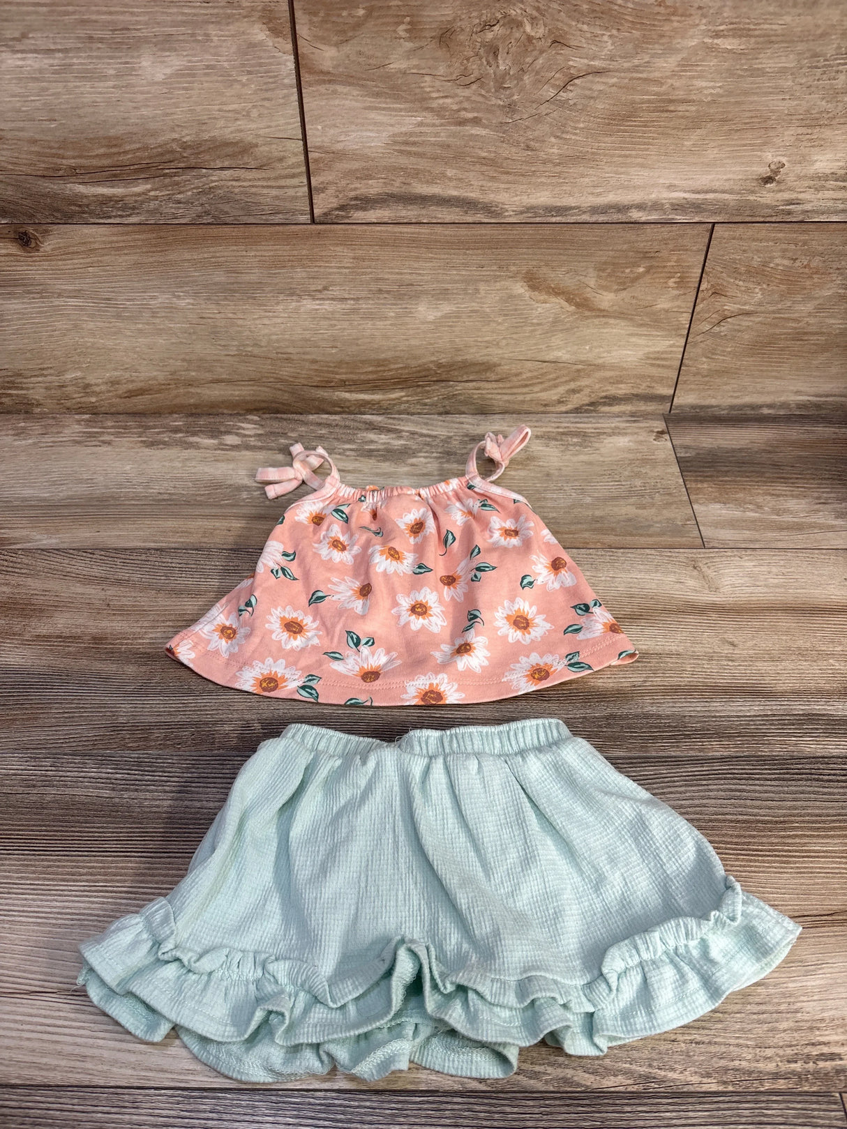 Flat lay of toddler tank top and shorts set showing pink floral tie-strap tank and mint ruffle shorts on wooden floor