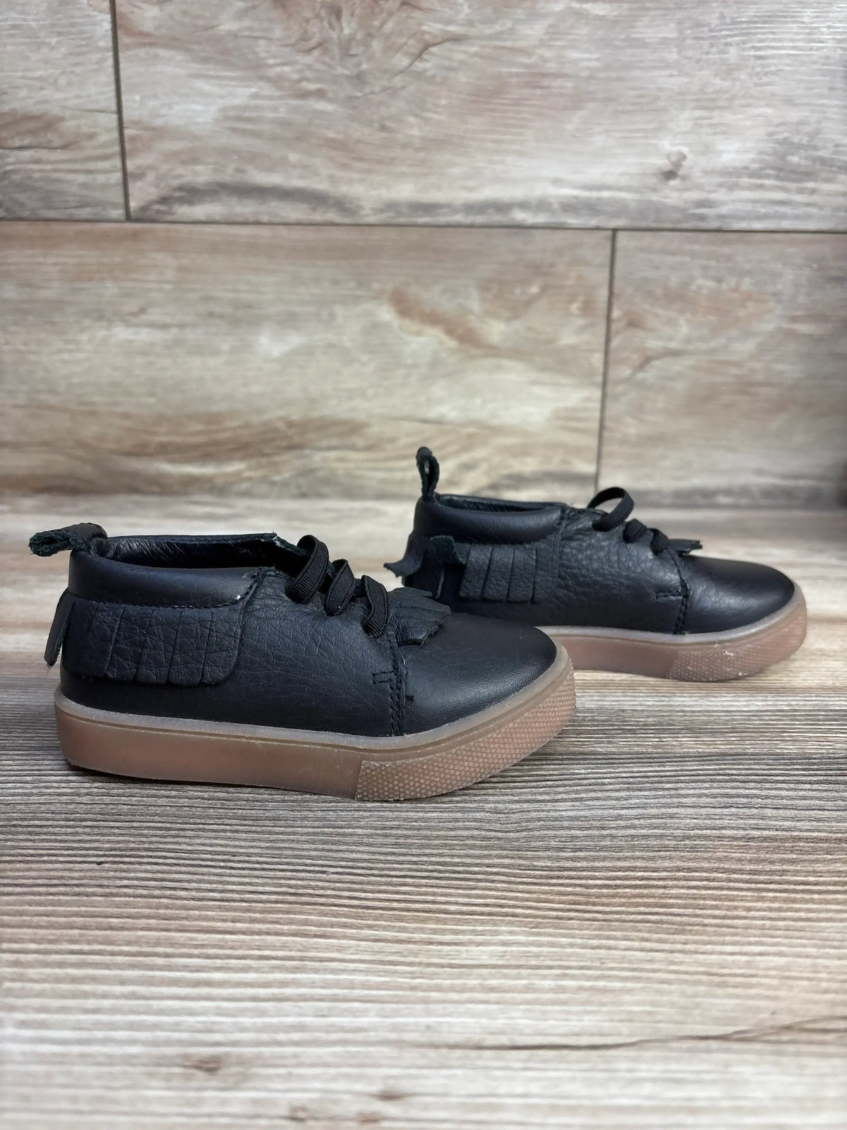 Black toddler fringe sneakers with brown sole on wood floor background