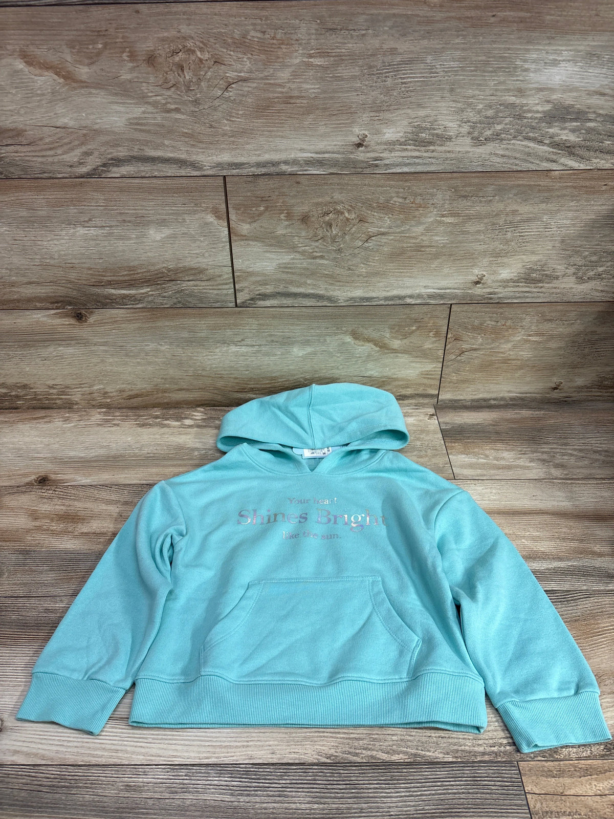 Front view of Cat and Jack aqua hoodie with kangaroo pocket and Your Heart Shines Bright Like the Sun chest text on a wood floor