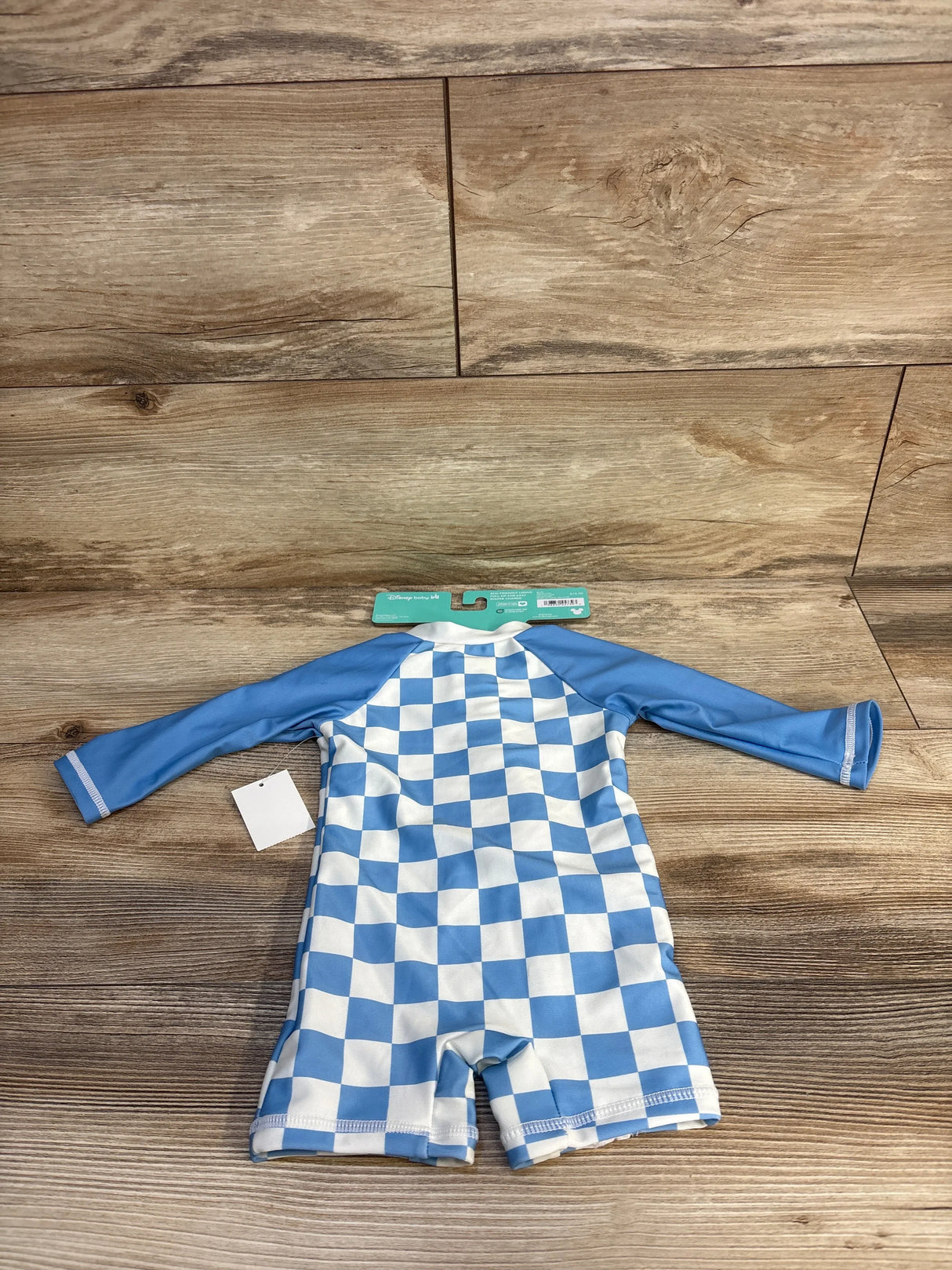 Blue and white checkered baby rash guard with long sleeves, Disney Baby tag, on wood floor