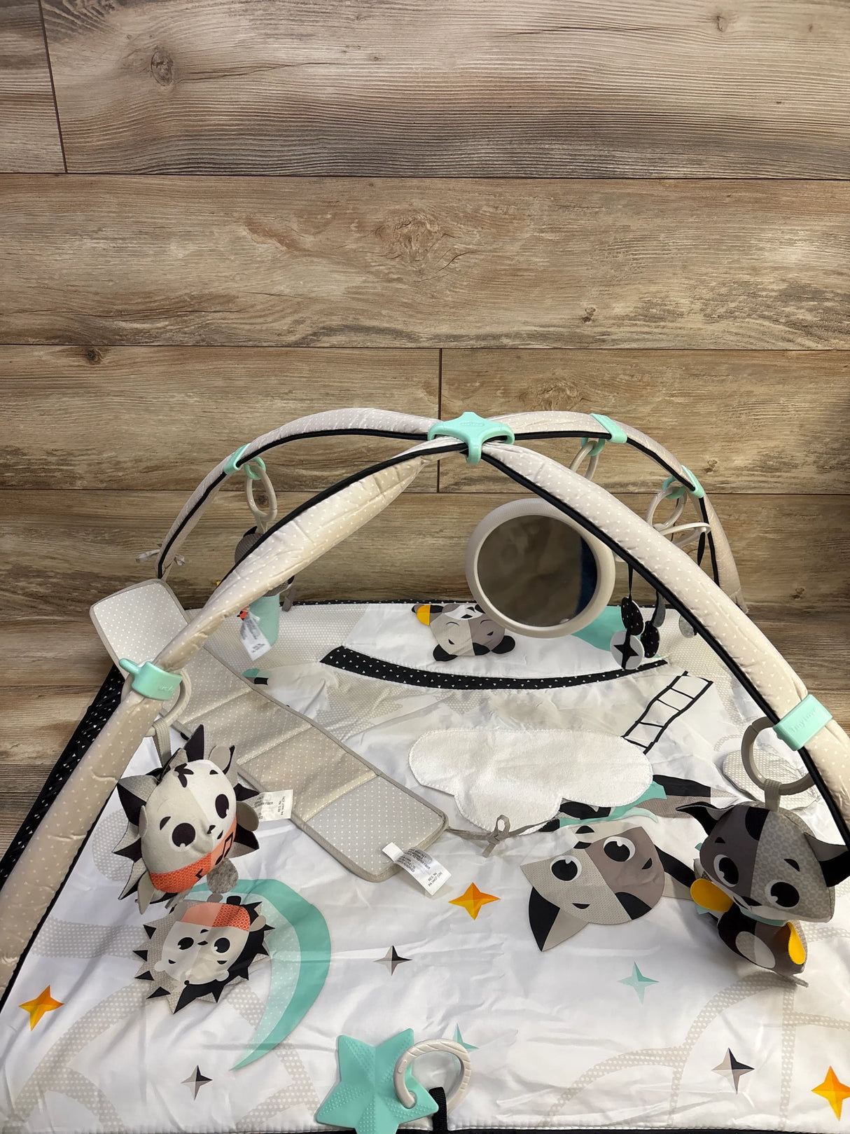 Top view of Tiny Love play gym with black-and-white mat, hanging toys and mirror on wood background