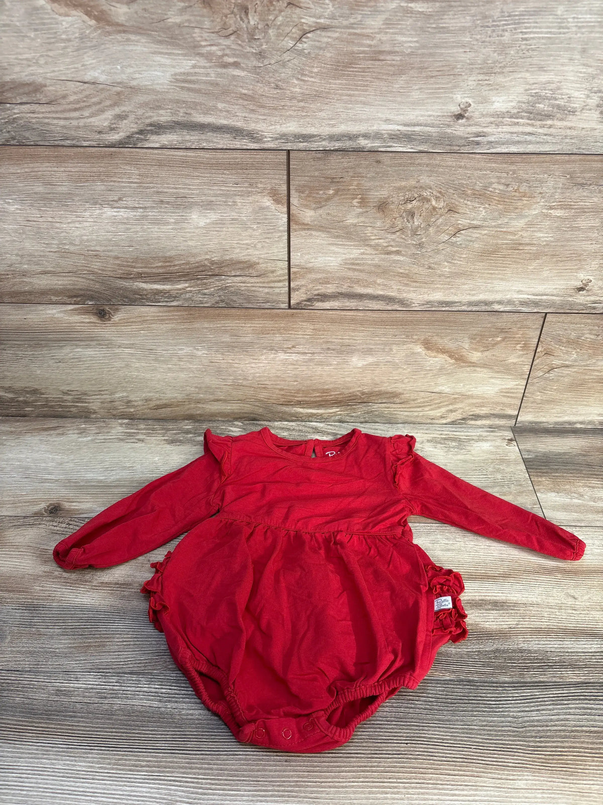 Front view of Ruffle Butts long sleeve ruffle bubble romper showcasing red fabric and ruffle details on a wood-grain background