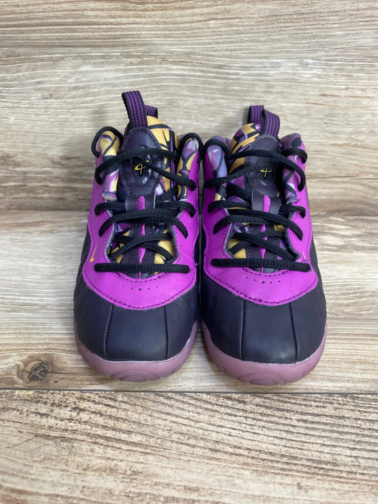 Front view of toddler Nike Little Posite One sneakers showcasing cave purple and black upper, patterned tongue and black laces on light wood background
