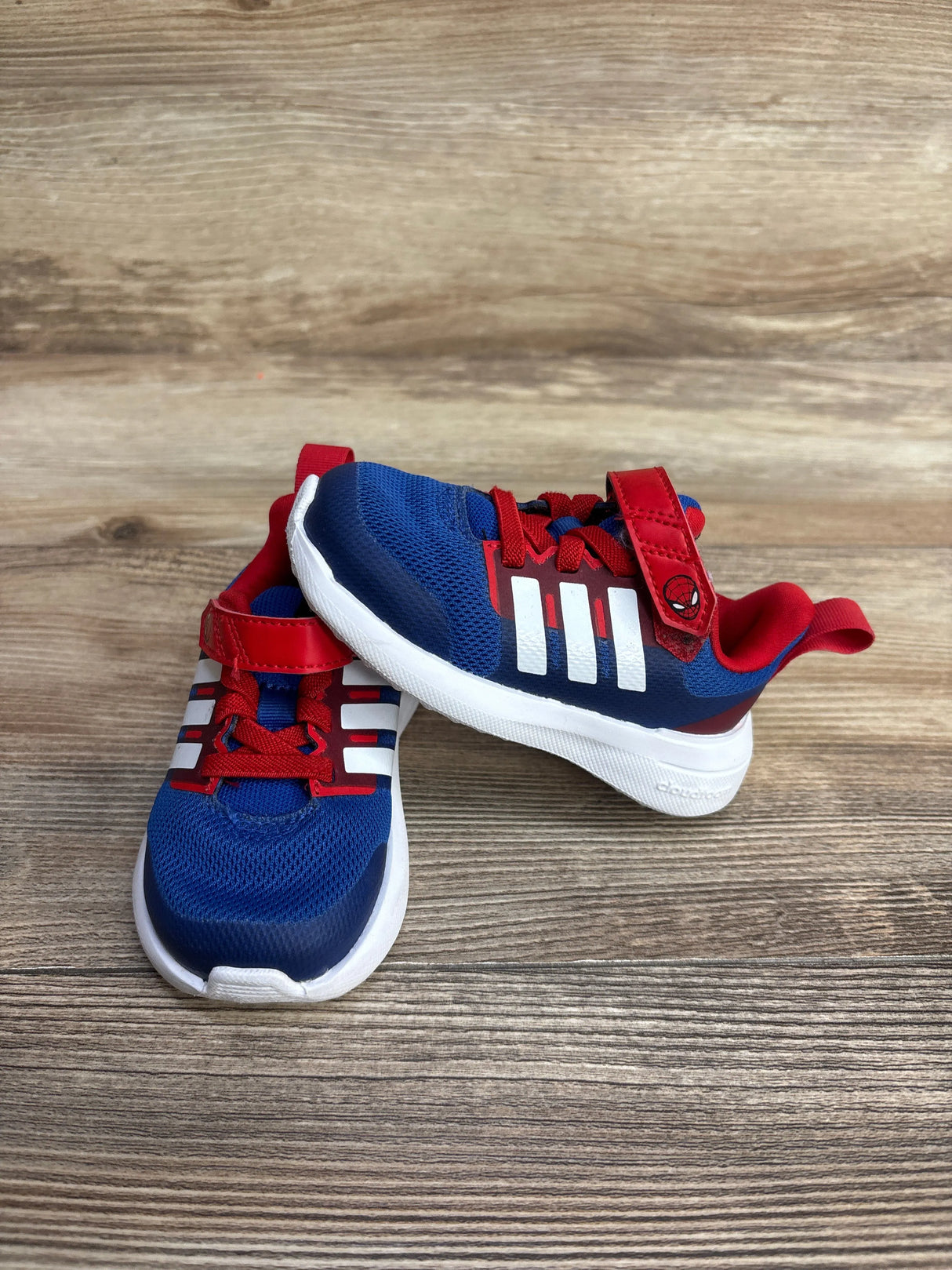 Blue and red toddlers' athletic sneakers with white soles and Spider-Man logo on wooden floor
