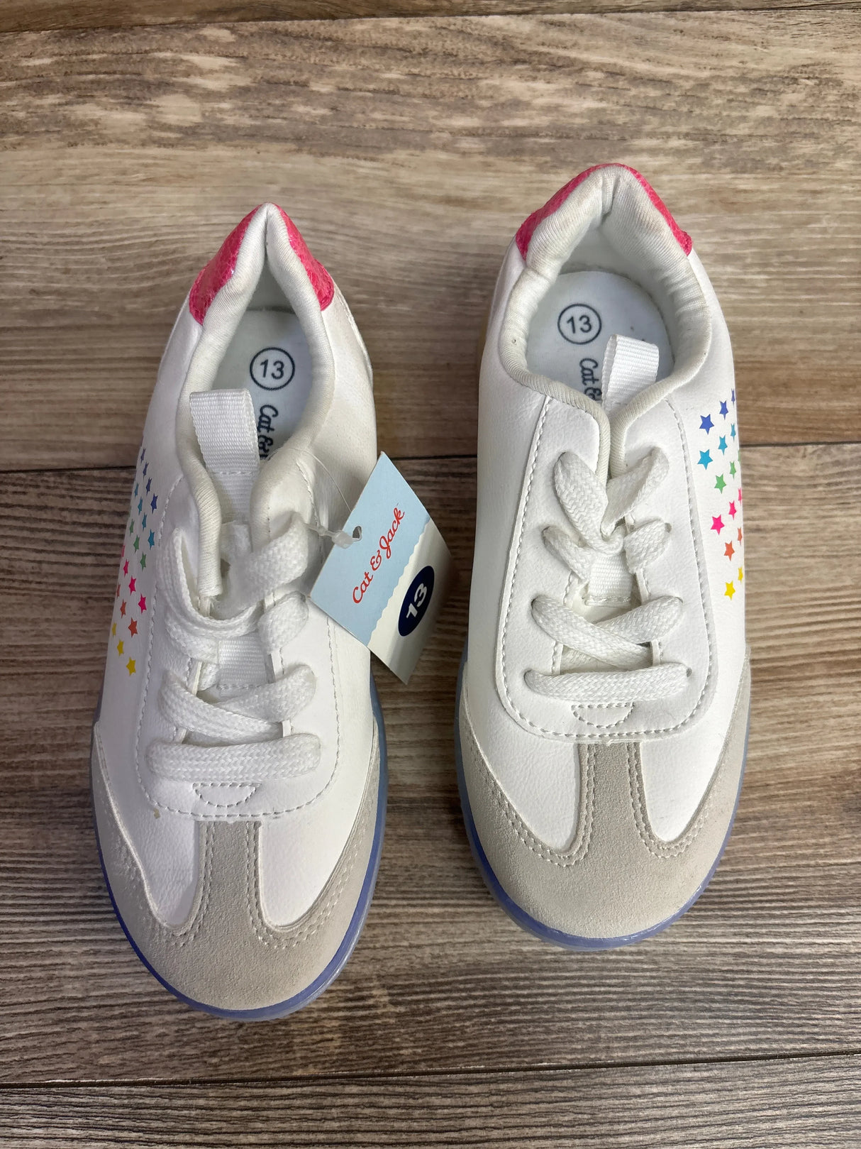 White toddler sneakers with rainbow stars, size 13, on wood floor
