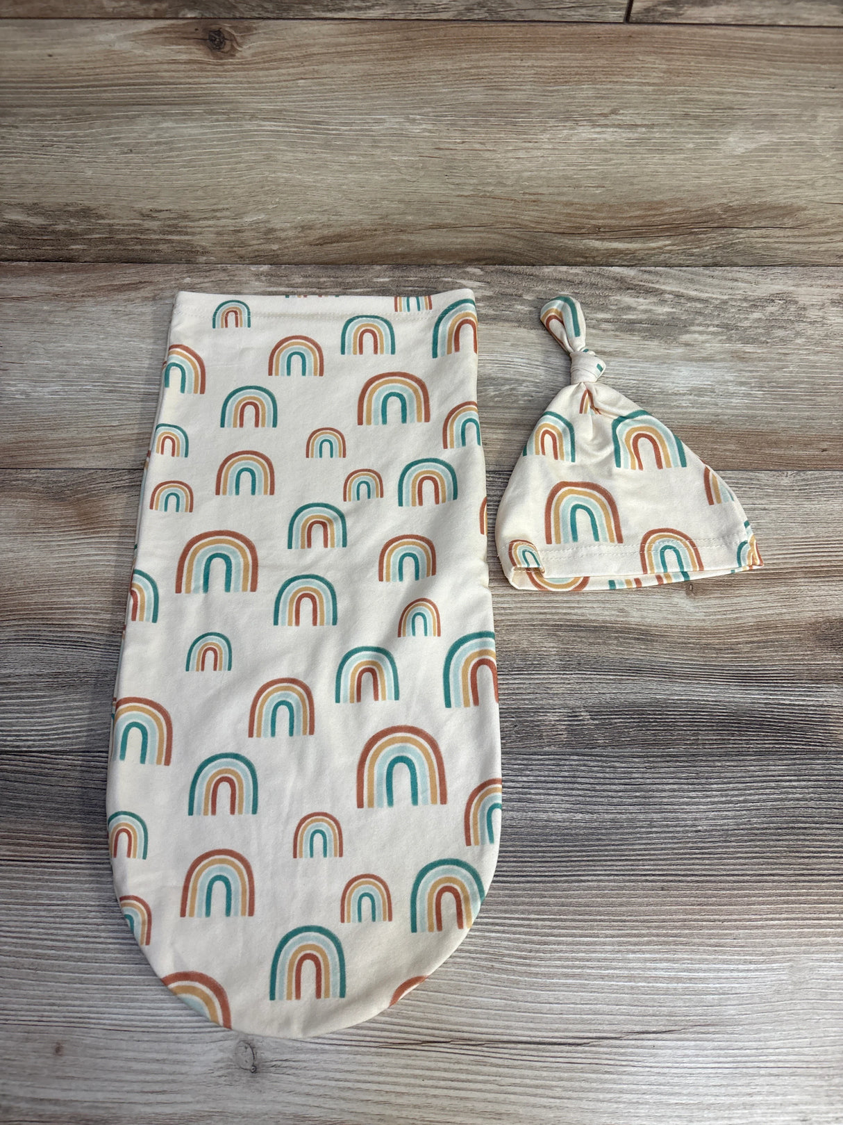 Baby swaddle and knotted hat set with colorful rainbow print on wooden background