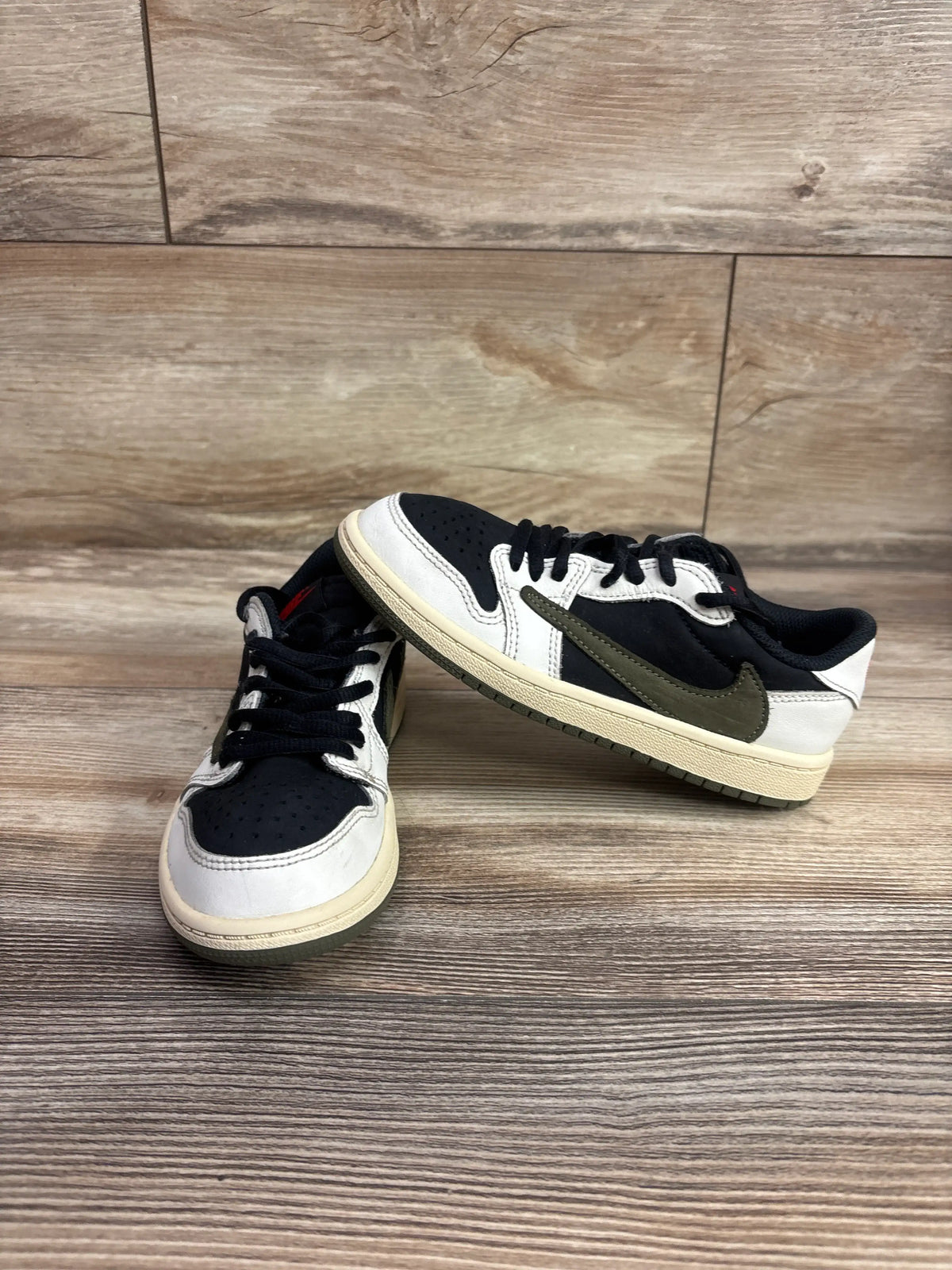 Angled view of Travis Scott x Air Jordan 1 Retro Low sneakers showcasing black white and olive color blocking on wood flooring