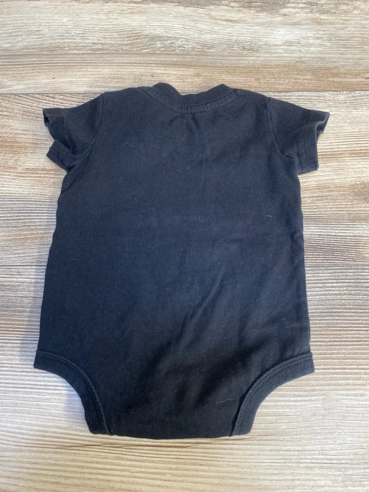 Black short sleeve baby onesie laid flat on wooden surface