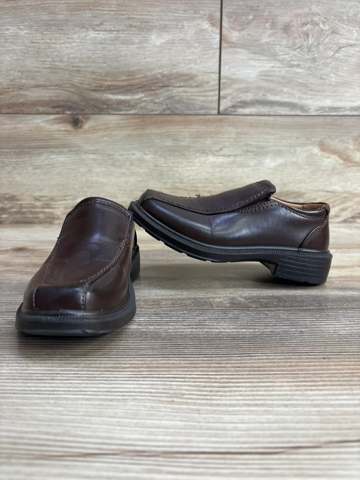 Pair of brown leather slip-on children's shoes on wood floor with wood panel background