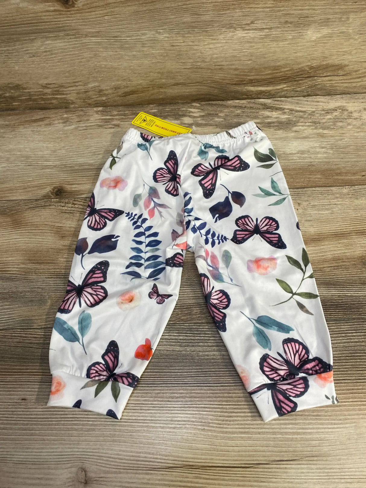 Flat-lay of white baby pants showing pink and navy butterfly print, elastic waistband and cuffed ankles on wood surface