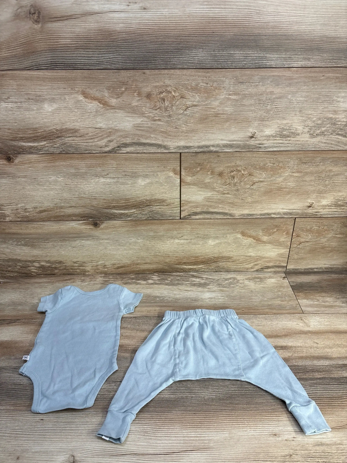 Top down view of light blue baby bodysuit and matching pants showing elastic waist and cuffed ankles on wood plank background