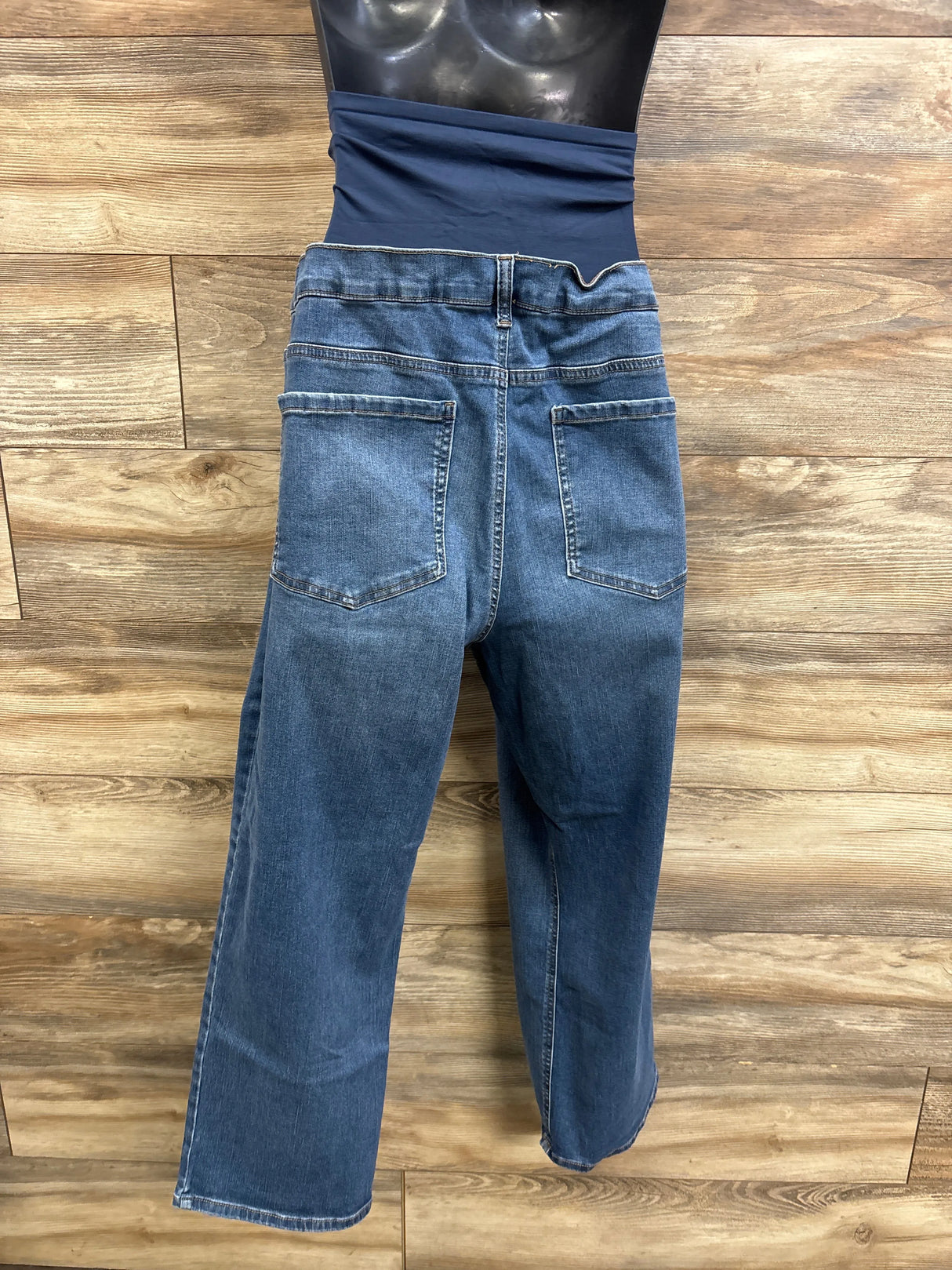 Back view of Time and Tru maternity blue jeans showing navy elastic belly panel, patch back pockets and straight legs on wood background