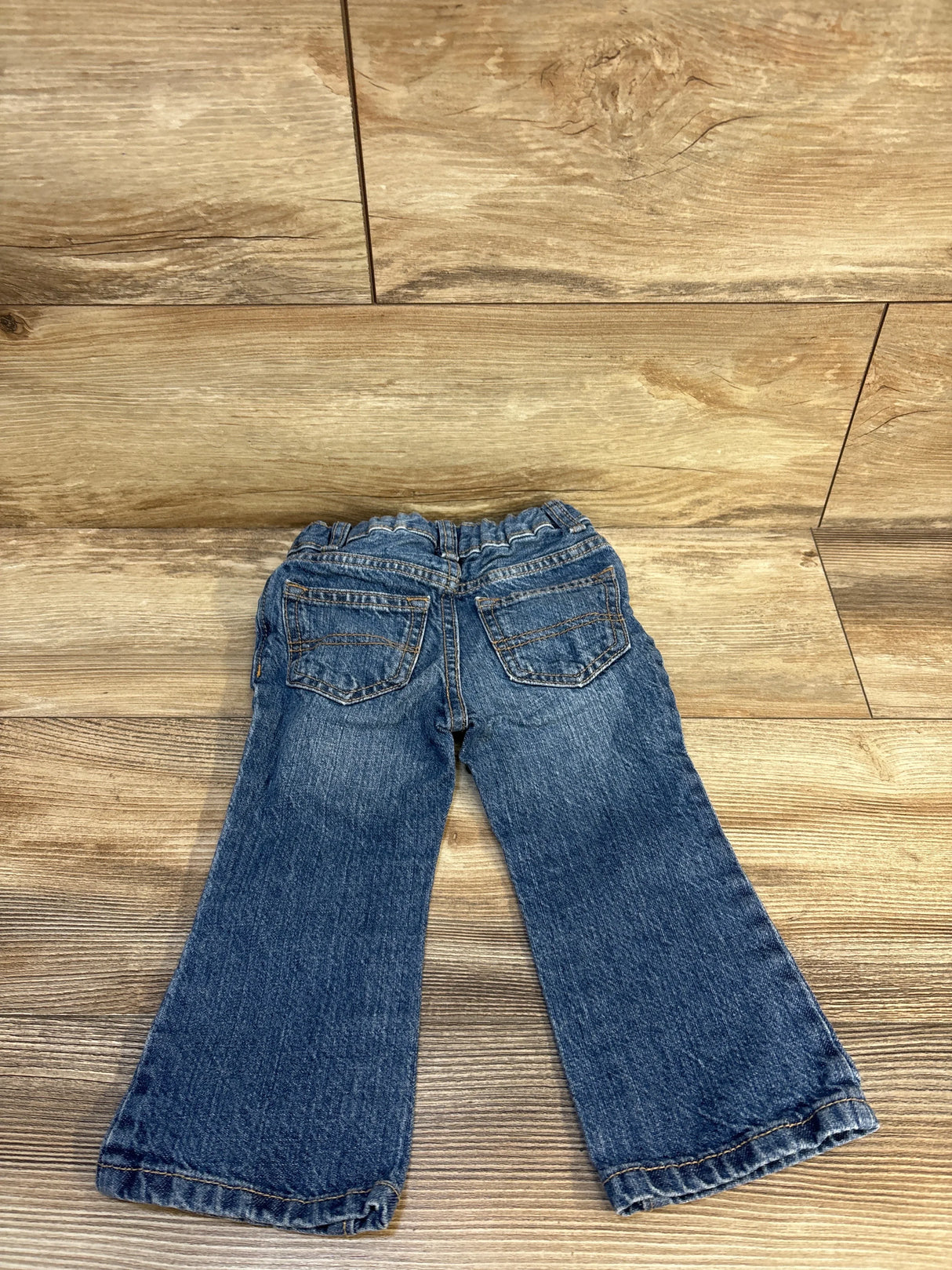 Rear view of blue toddler jeans with elastic waistband on wood floor
