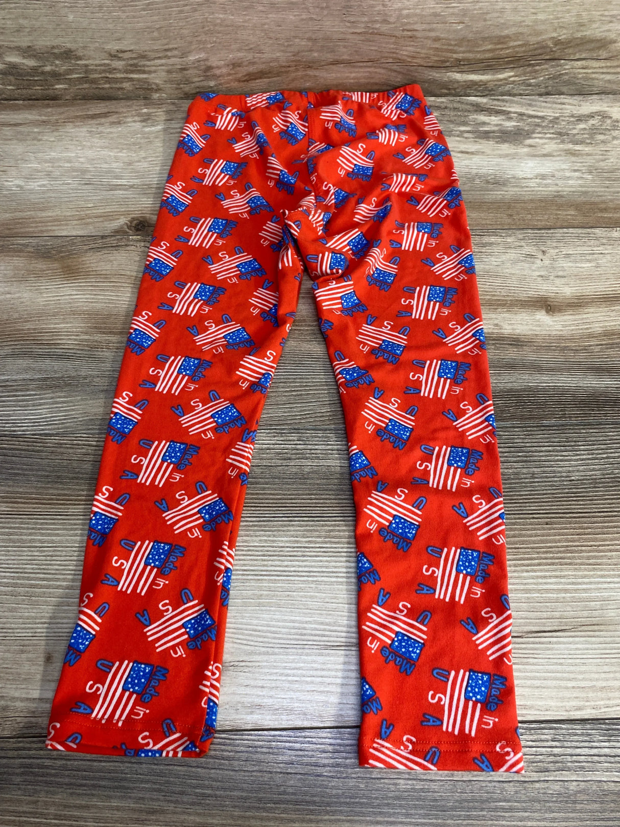 Flat-lay of red toddler leggings size 5/6 showing all-over blue and white Made in USA flag print on wood floor background