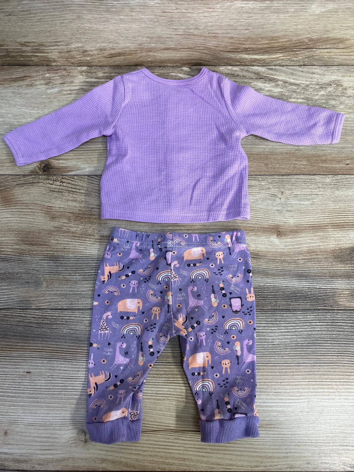 Flat lay of lilac waffle-knit baby top and pants set with horse embroidery on top and animal-print pants on wood background