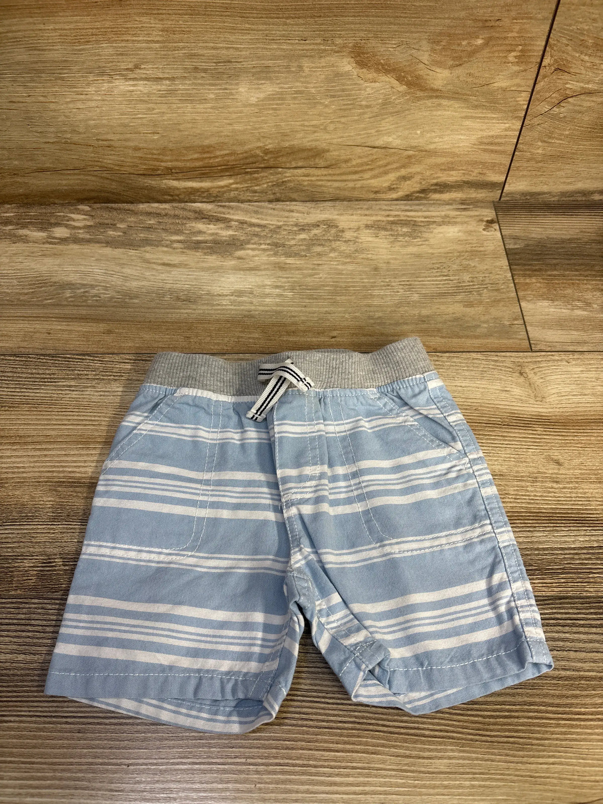 Front view of Nautica striped drawstring shorts showcasing blue and white horizontal stripes, elastic waistband, and pockets on a wood floor