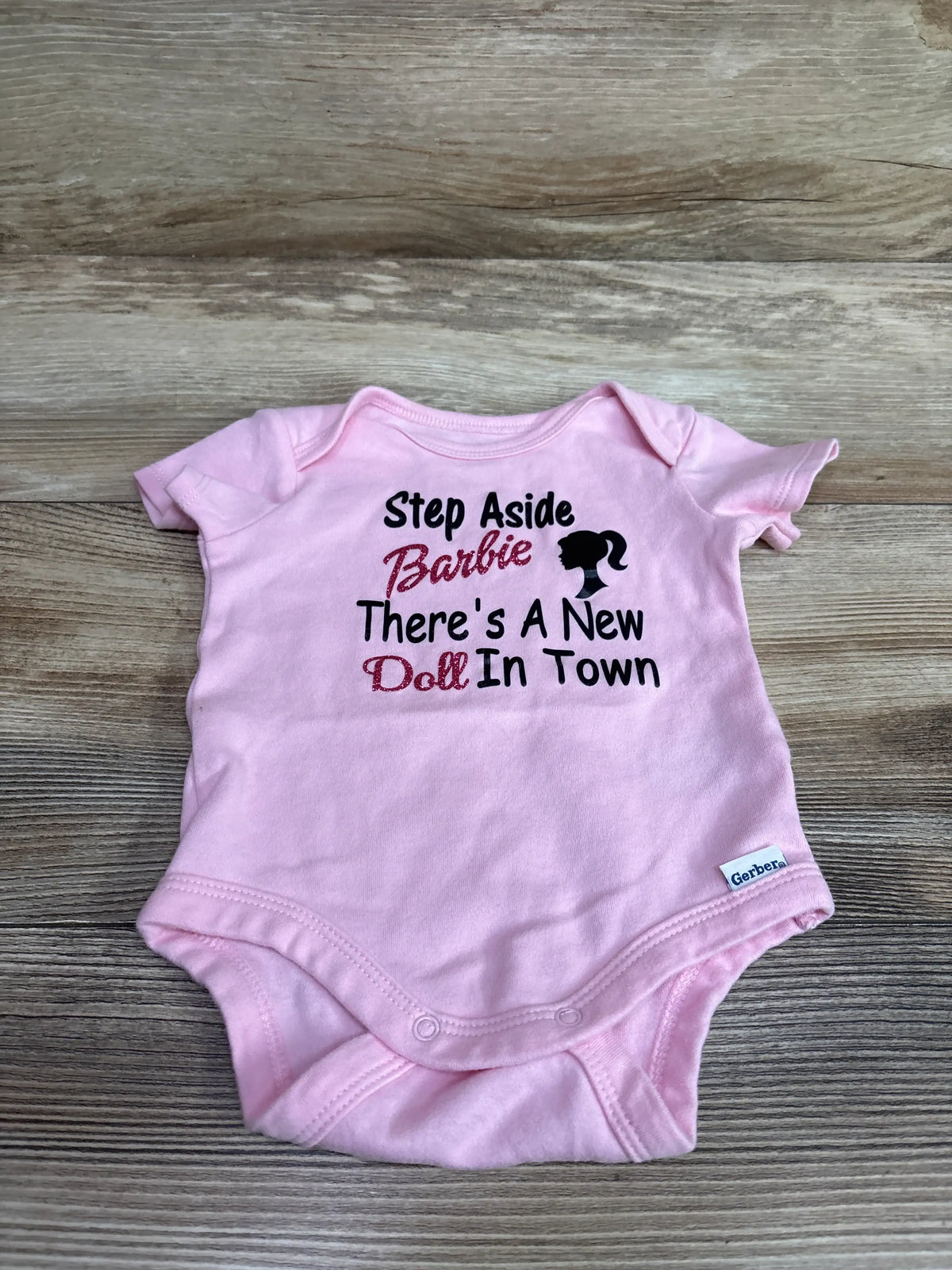 Pink Gerber bodysuit with 'Step Aside Barbie There's A New Doll In Town' text and silhouette.