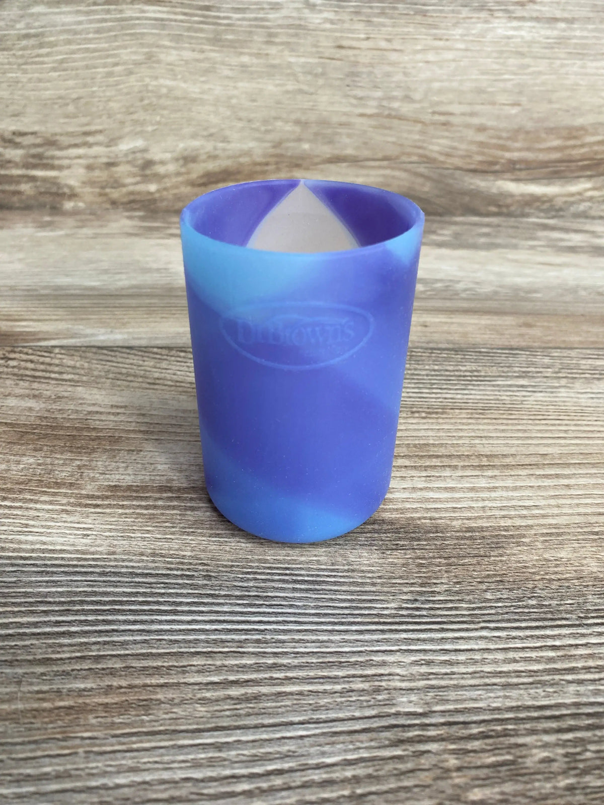 Front view of Dr. Brown's Options+ 4 oz bottle sleeve showing purple-blue glow-in-the-dark silicone with embossed Dr. Brown's logo on wood background