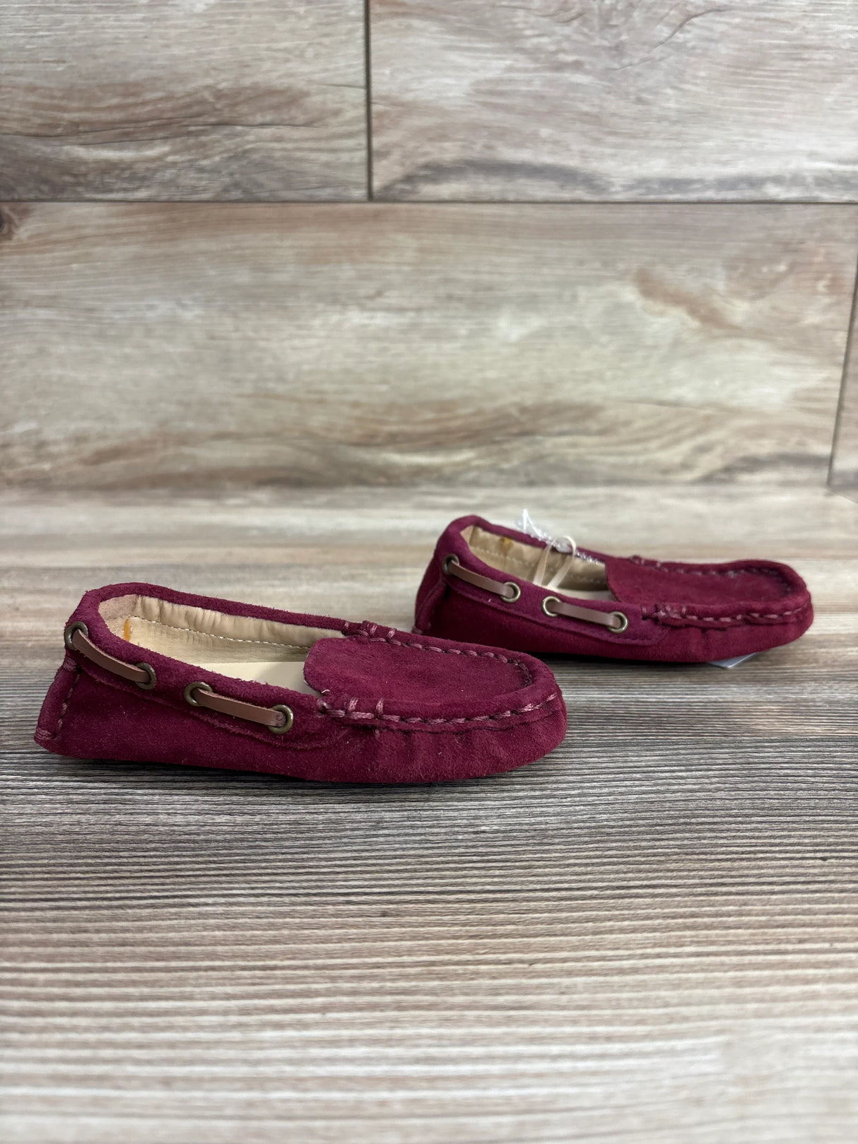 Pair of burgundy suede moccasin loafers for kids with brown lace detail, displayed on wood surface