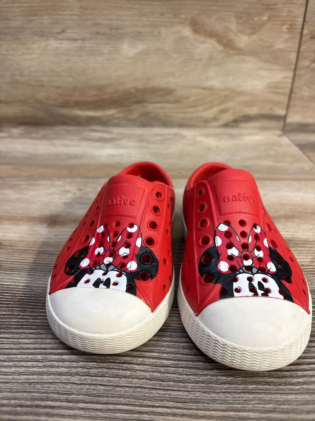 Front view of red Jefferson slip-on toddler shoes with painted Minnie Mouse faces and white toe caps on wood