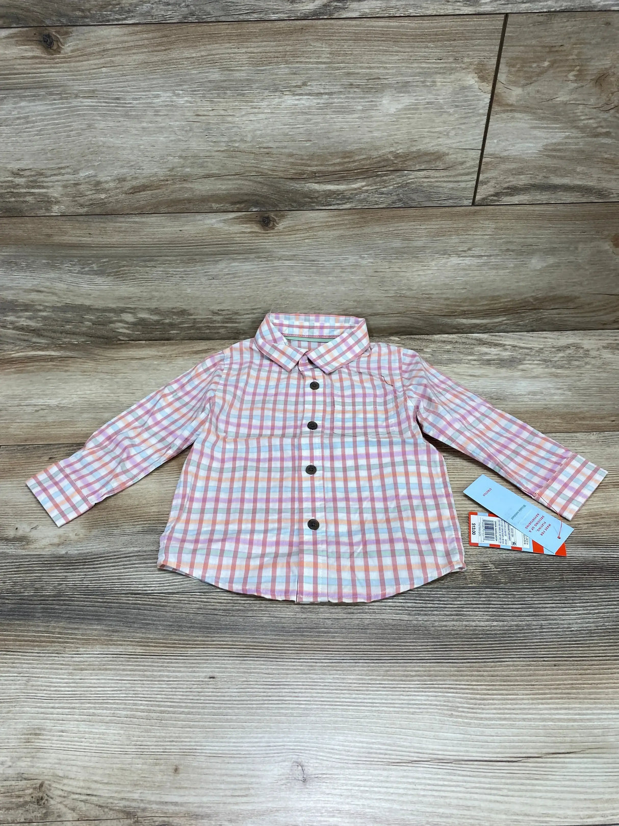 Front view of toddler pink and white plaid button-up shirt showcasing dark buttons, spread collar, long sleeves, tags attached on wood background