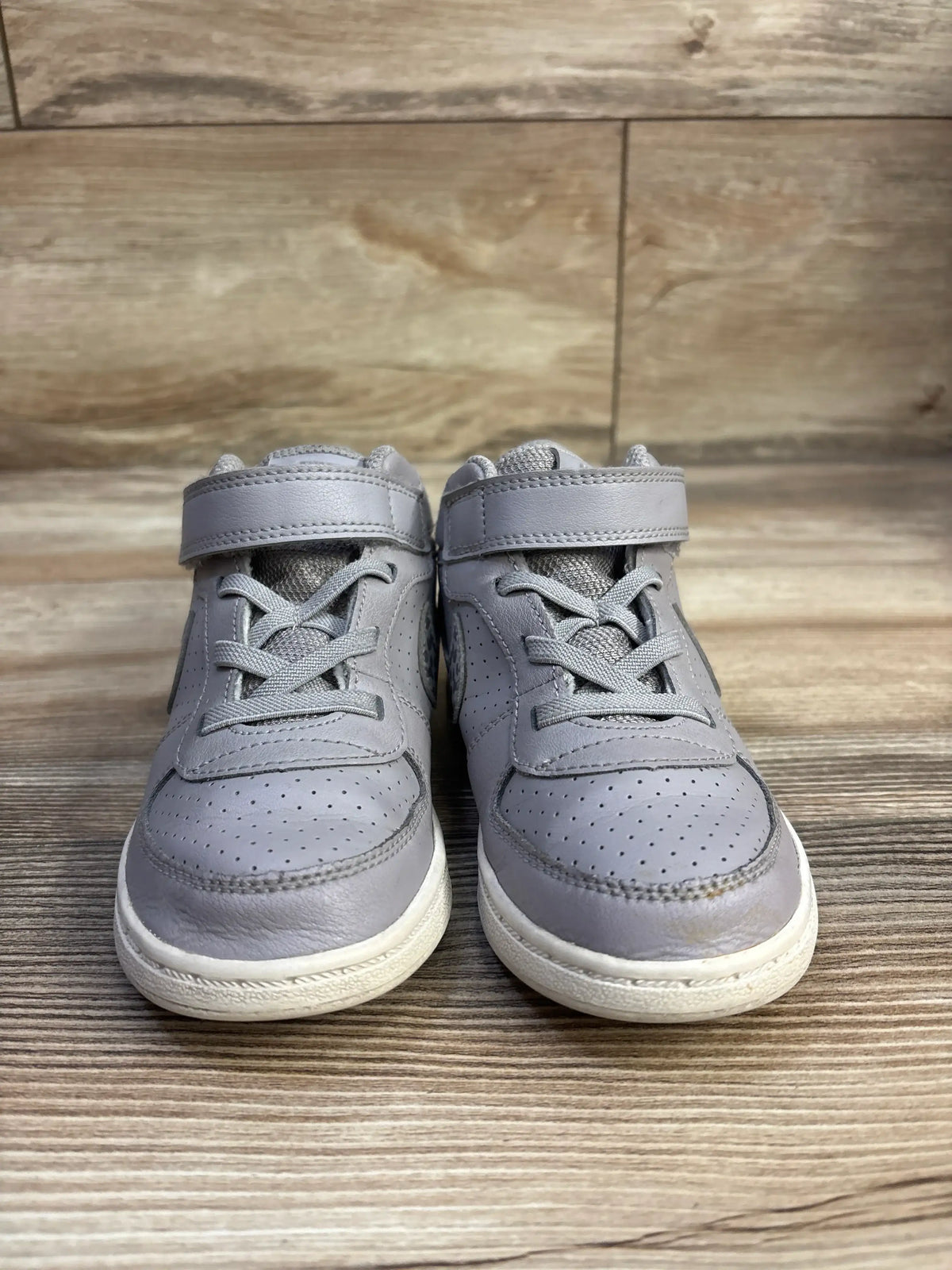 Front view of Nike Court Borough Mid toddler sneakers in grey with Velcro strap, perforated toe, and white sole on wood background