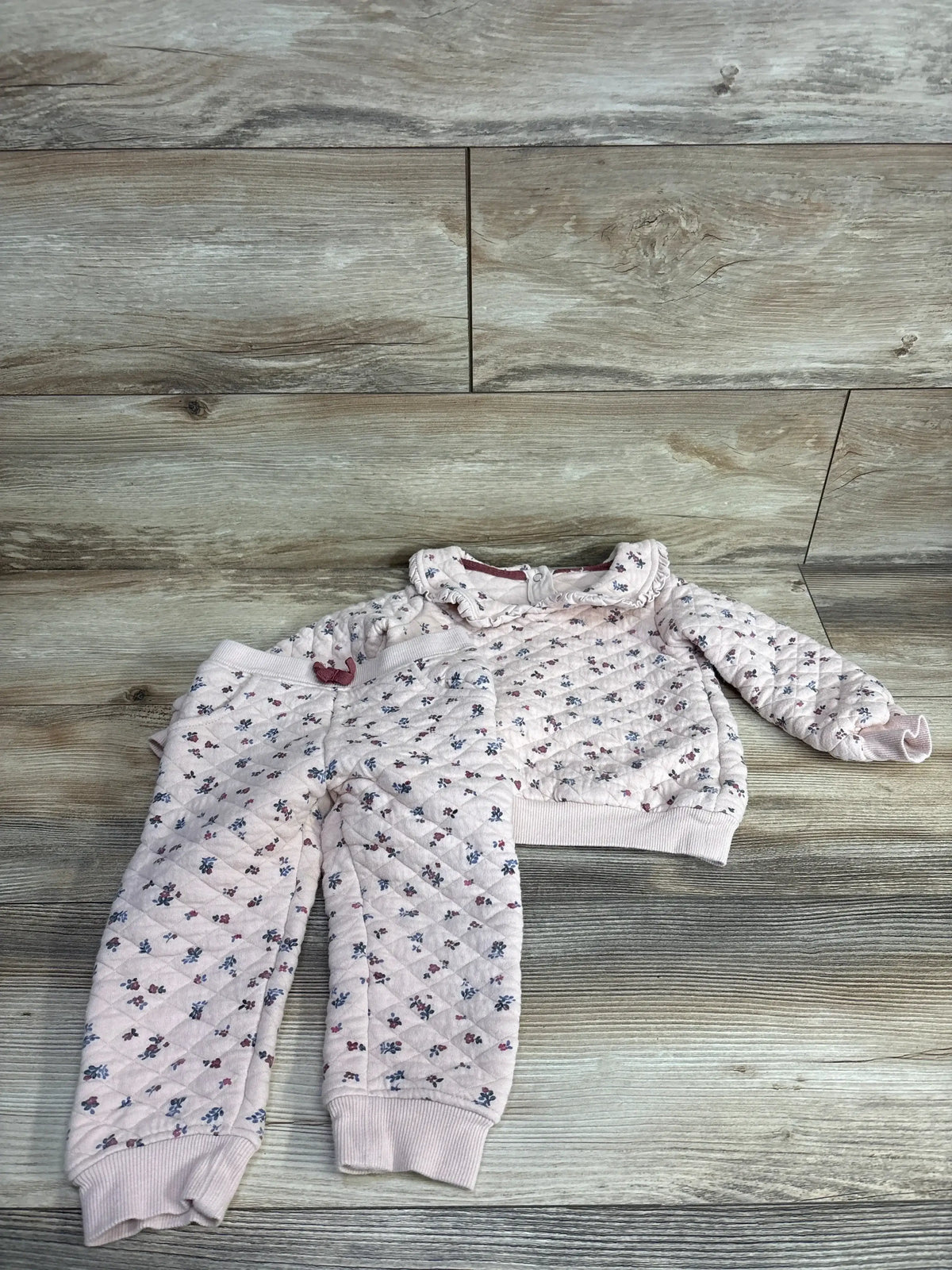 Pink quilted toddler outfit with floral print, includes pants and long-sleeve top on wood floor