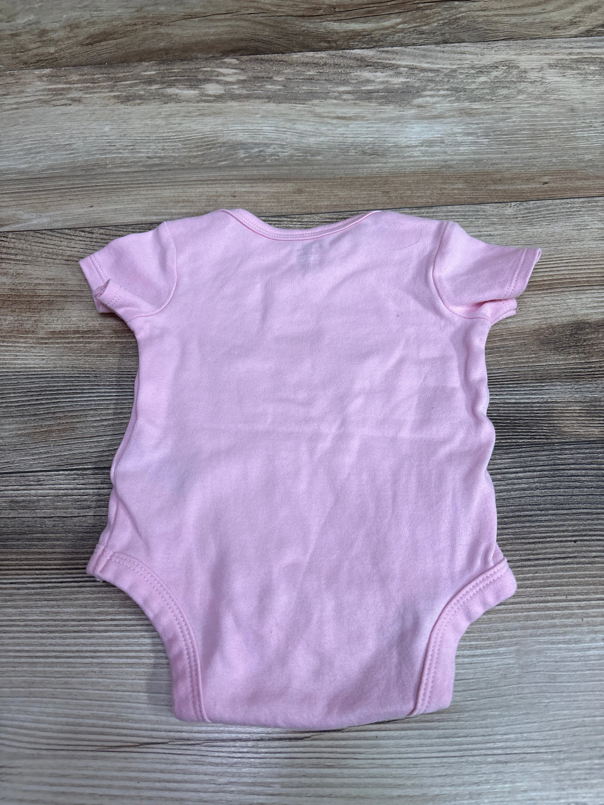 Back view of pink Gerber baby bodysuit with short sleeves on a wood-grain background