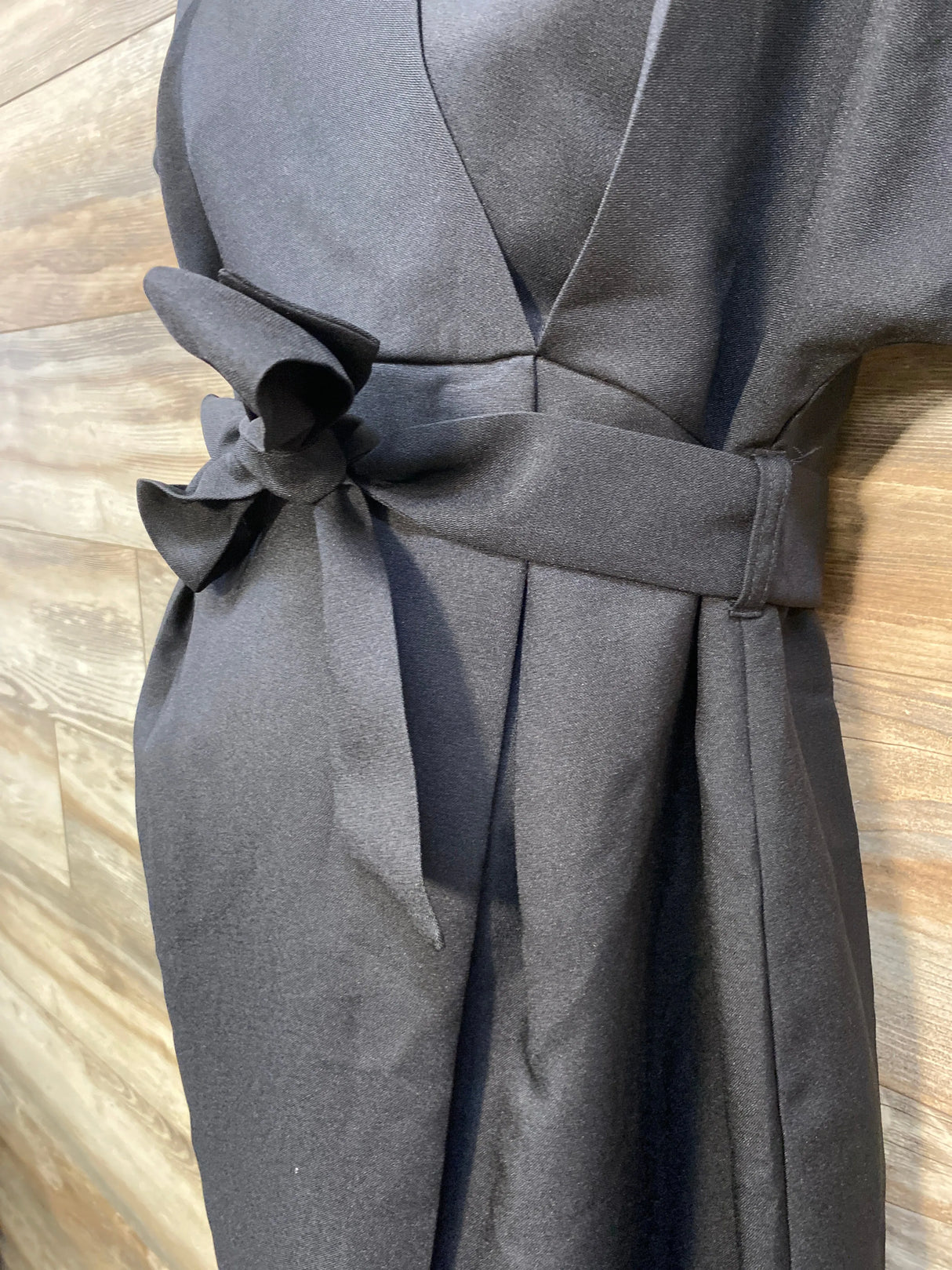 Black dress with waist belt bow against wood panel wall