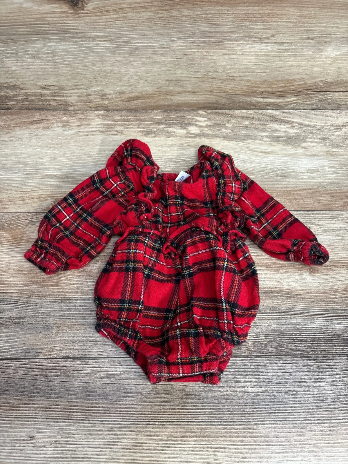 Red plaid baby romper with ruffled sleeves and legs, laid on wood floor
