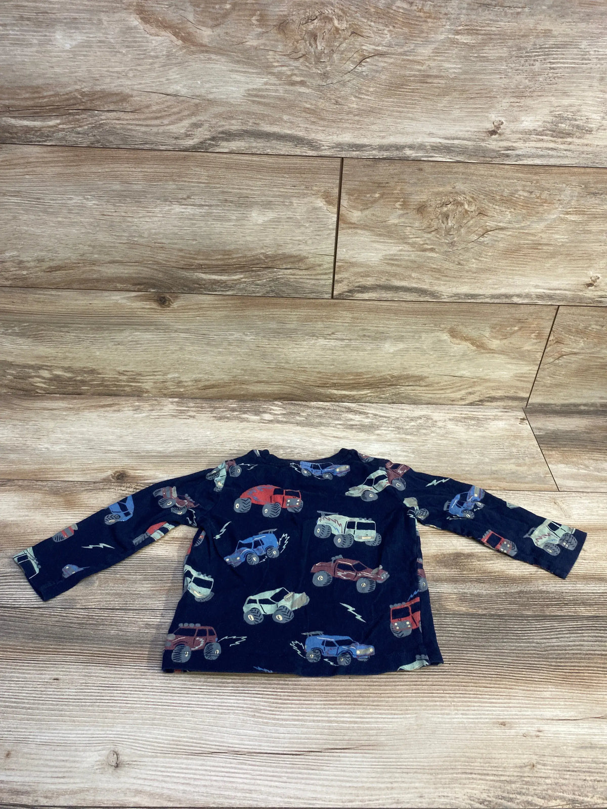 Front view of navy Baby Gap long-sleeve toddler shirt showcasing all-over monster truck print laid flat on wood floor background