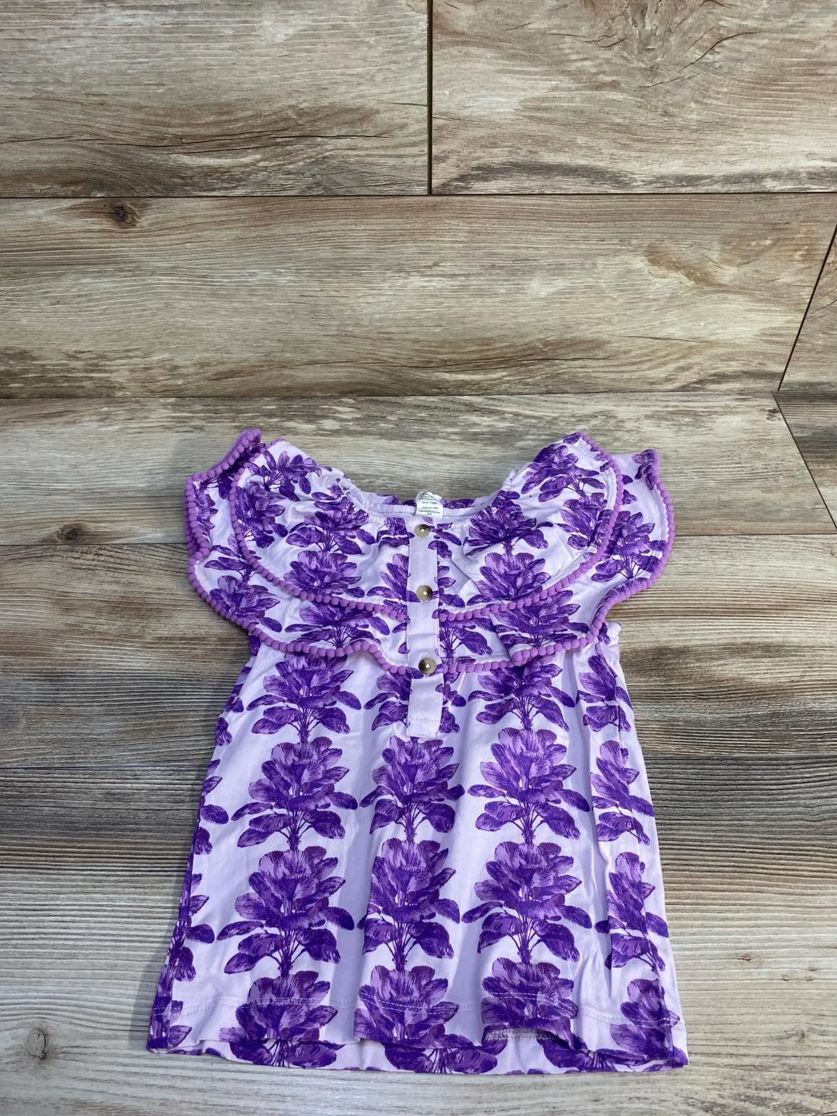 Flat lay of purple ruffle henley top (4T) showing ruffled yoke and front buttons on wood background
