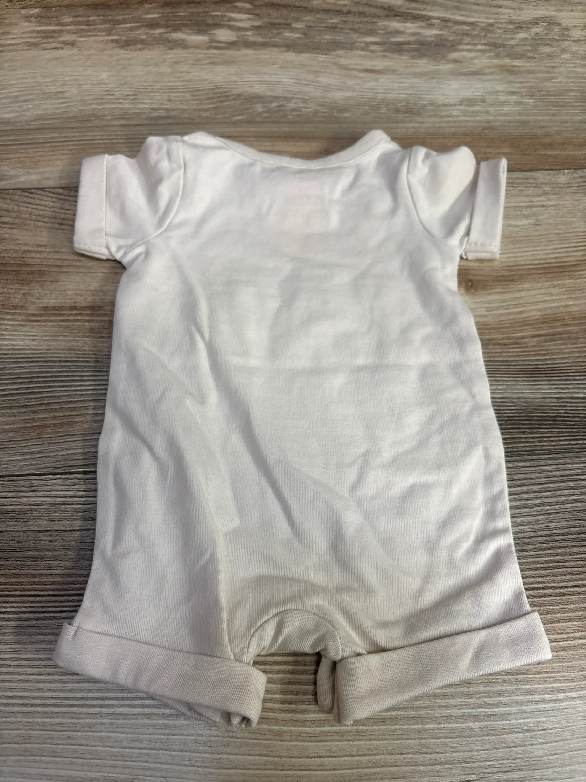 White baby romper with rolled sleeves and leg cuffs on wooden background
