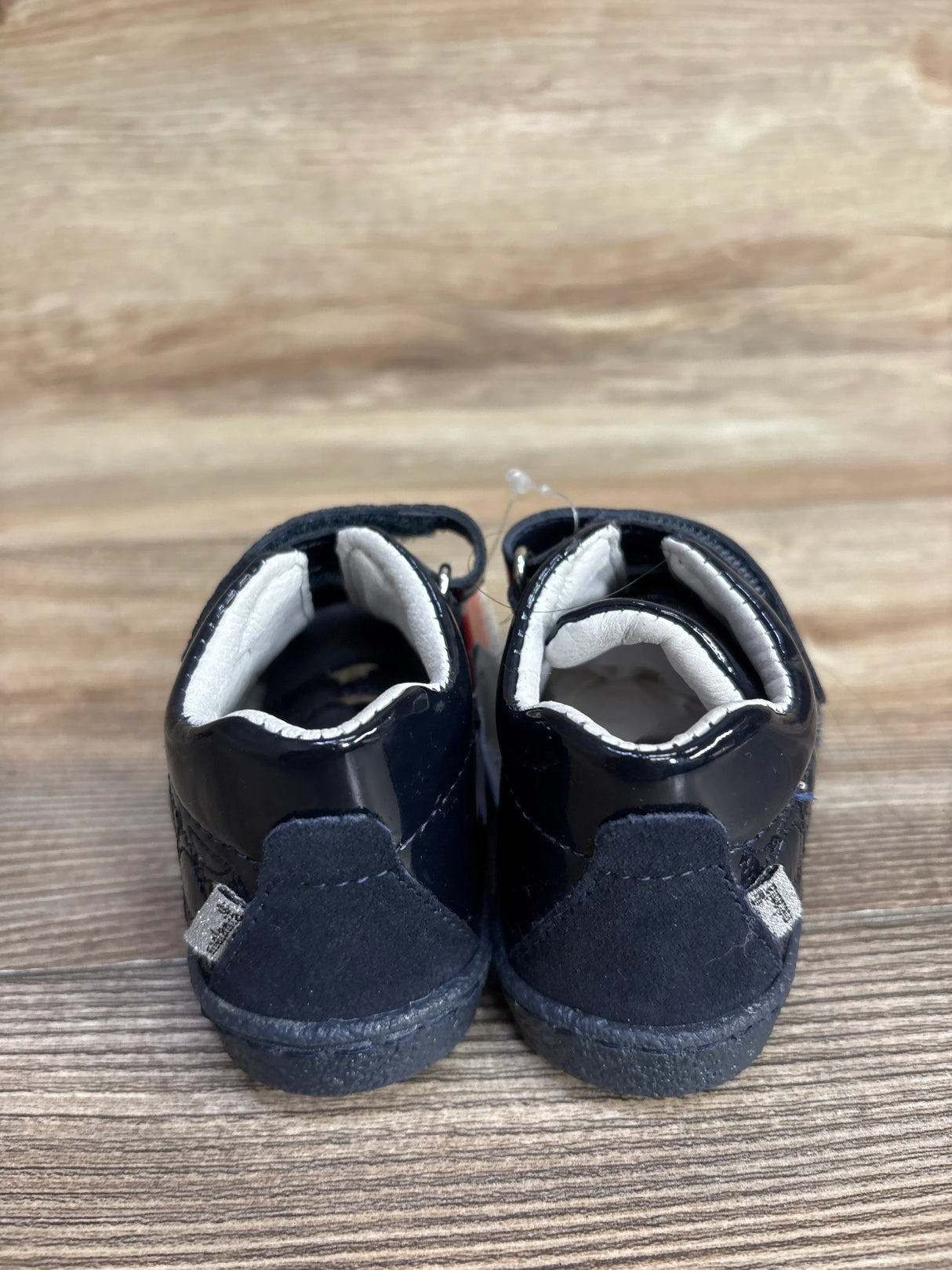Back view of small black baby shoes on wooden surface with cushioned white interior