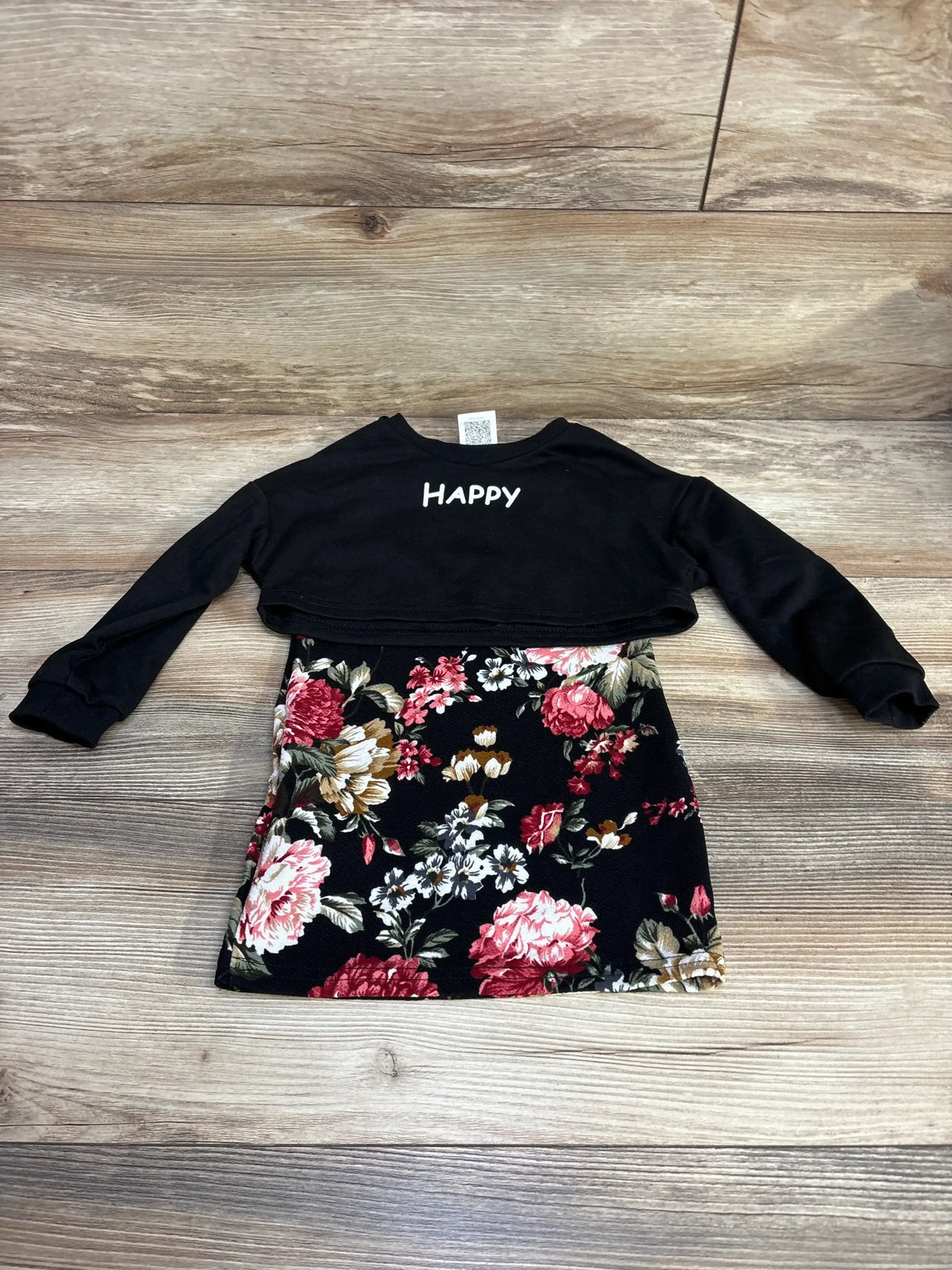 Flat lay of toddler black cropped long-sleeve top and floral skirt set showcasing HAPPY back print on wood background