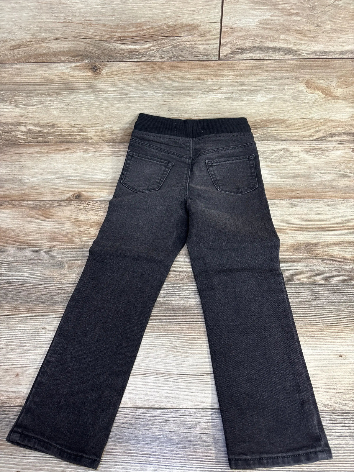 Black kids' jeans with elastic waistband and back pockets on wood floor