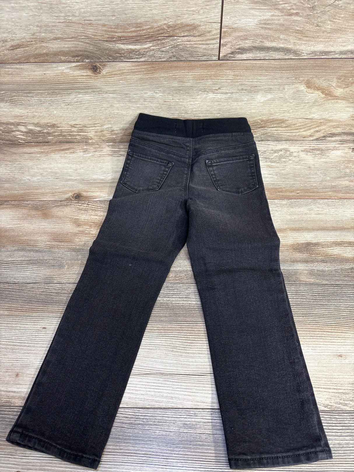 Black kids' jeans with elastic waistband and back pockets on wood floor