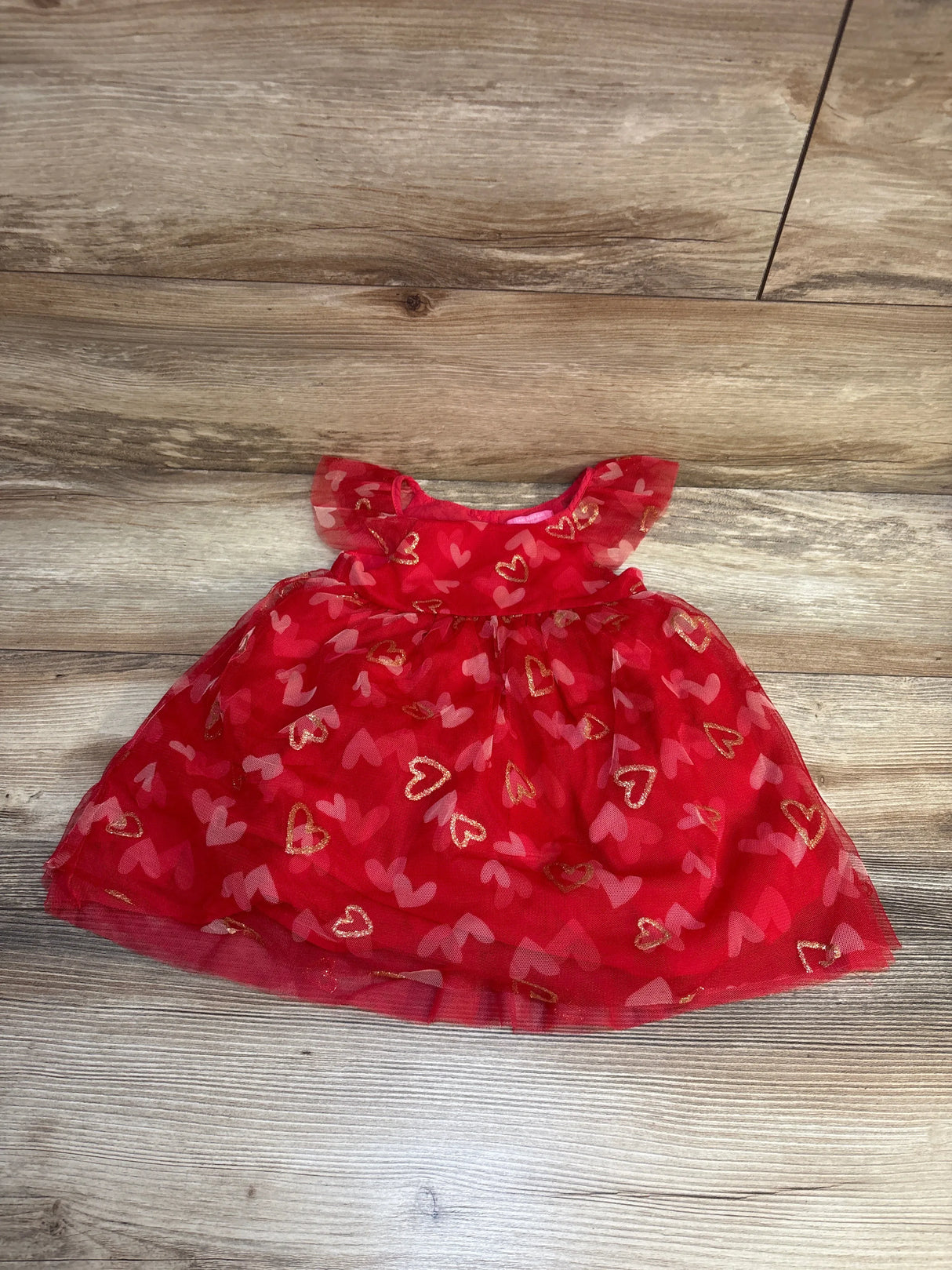 Red baby dress with gold and pink heart patterns on wooden floor